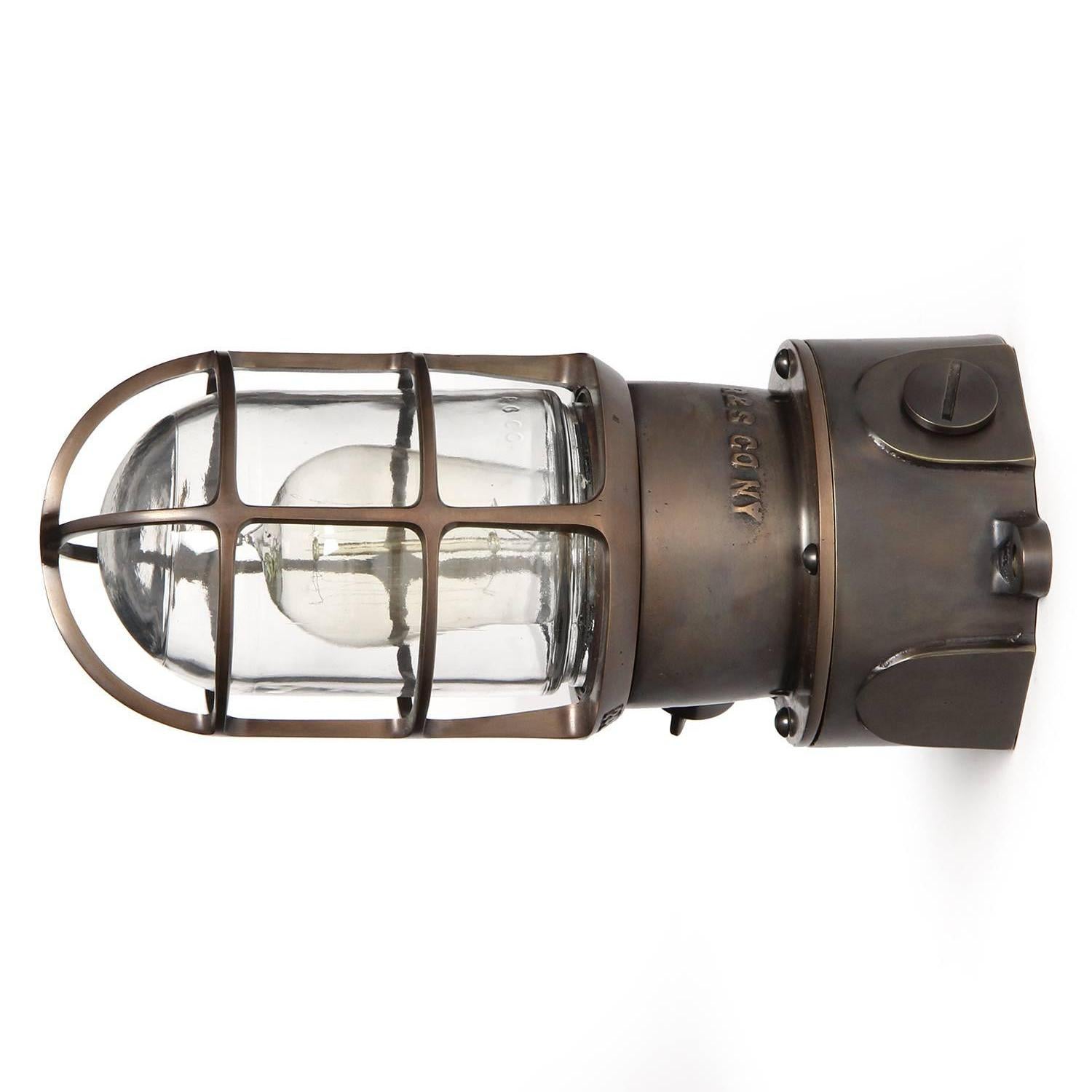 A superb quality industrial caged flush mount light fixture in patinated cast bronze with a thick clear glass diffuser.