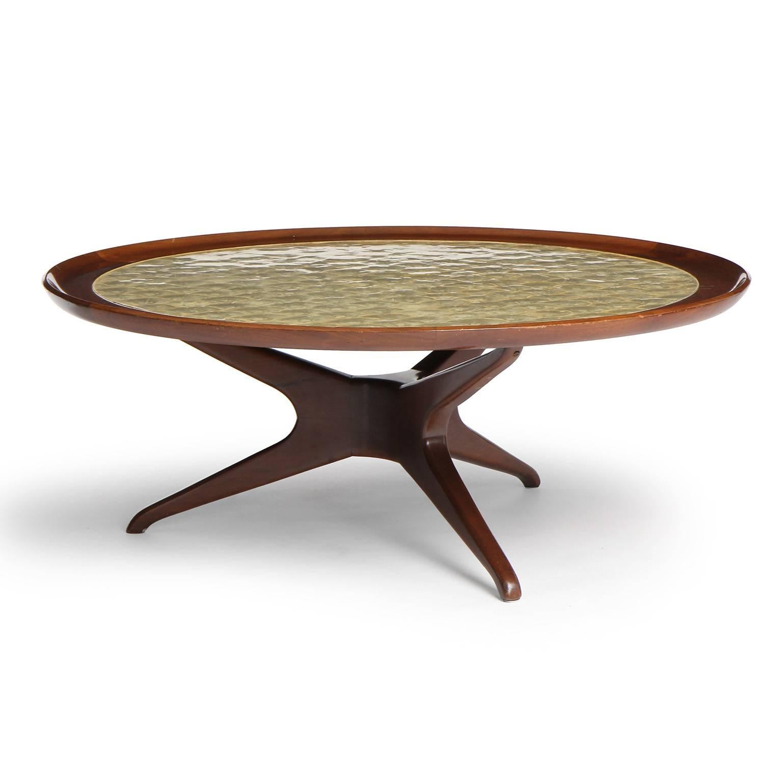 An impressive walnut low round table having a sculptural three-legged base supporting a floating top masterfully surfaced with inset scalloped capiz shells.  