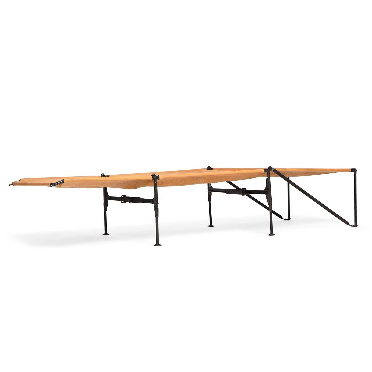 A spare and interesting folding cot having an architectural wrought iron structure and a thick natural hand stitched leather surface.