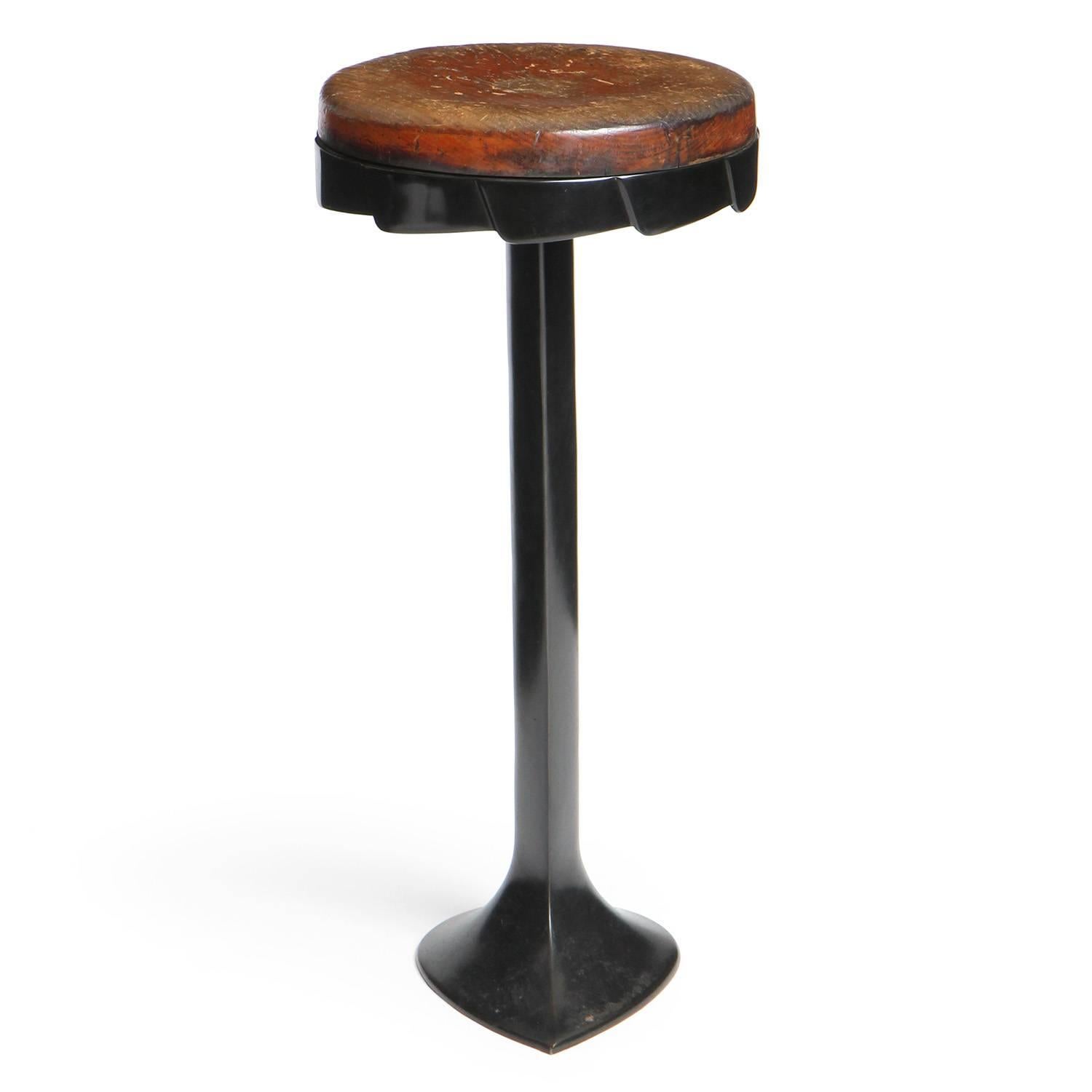 A patinated cast iron barstool with a dished wooden swivel seat and 