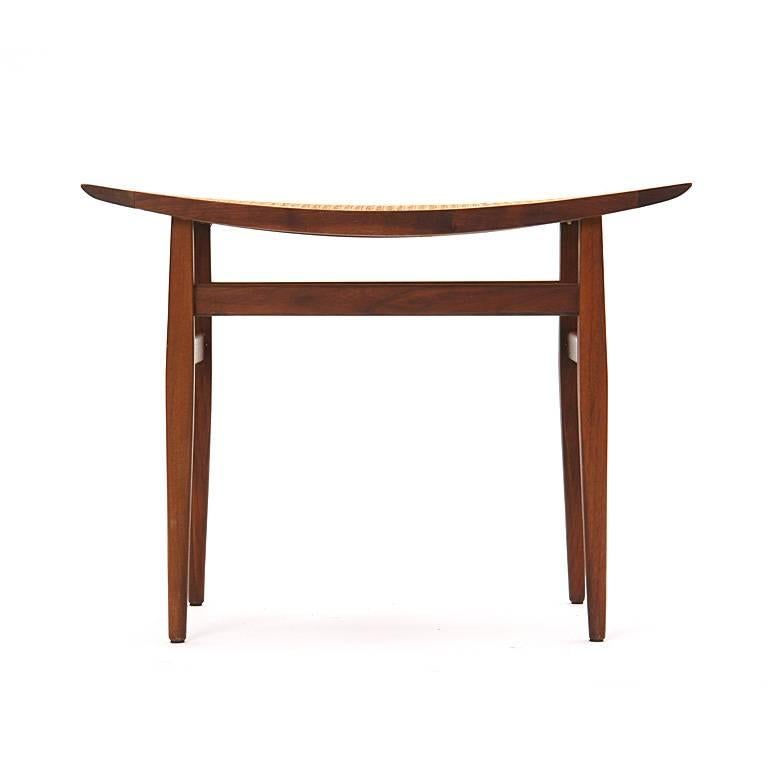 A walnut stool with a swayed, caned seat on tapered legs.