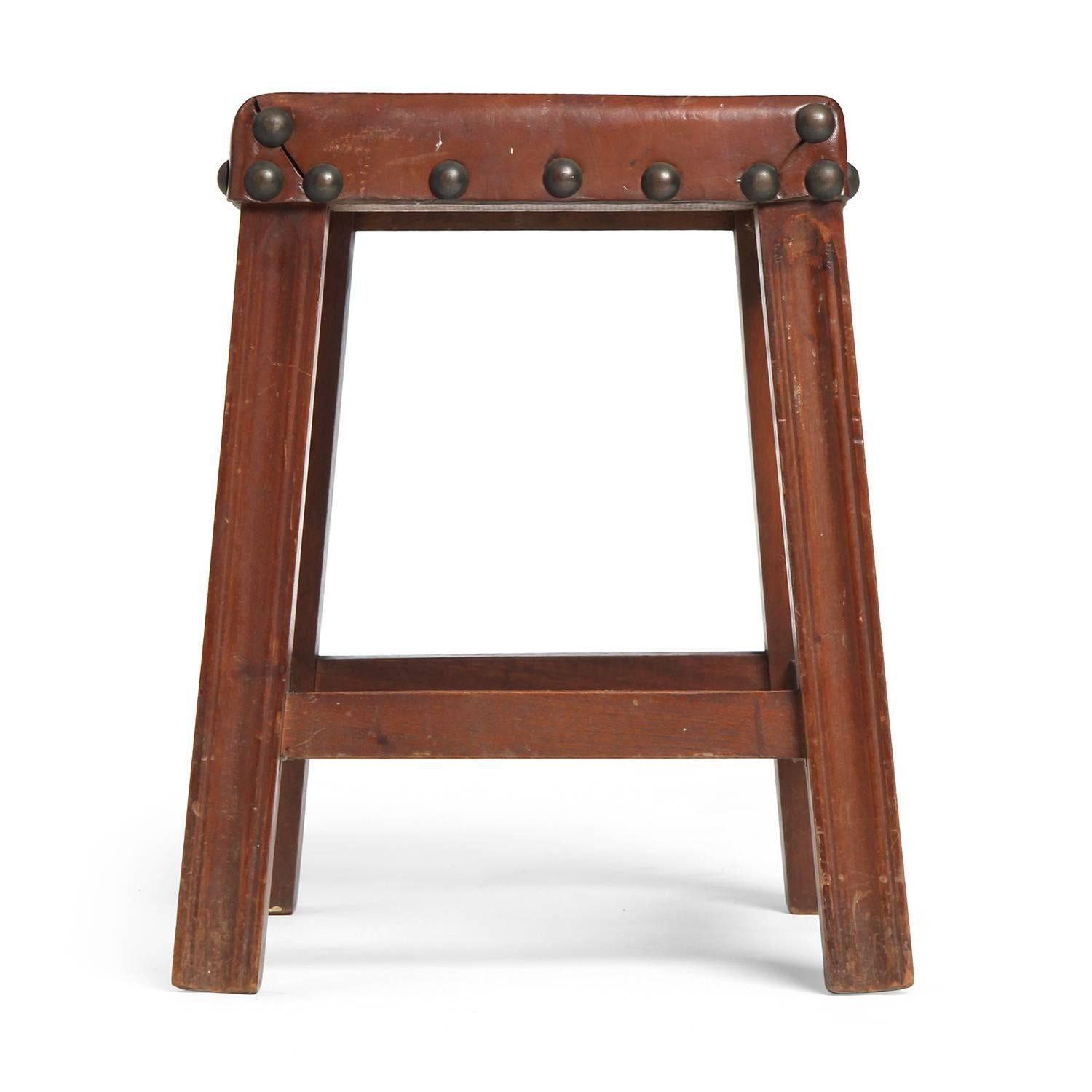 A substantial and finely executed low stool having a flaring square walnut frame and a thick burgundy leather seat with expressive nail head trim.