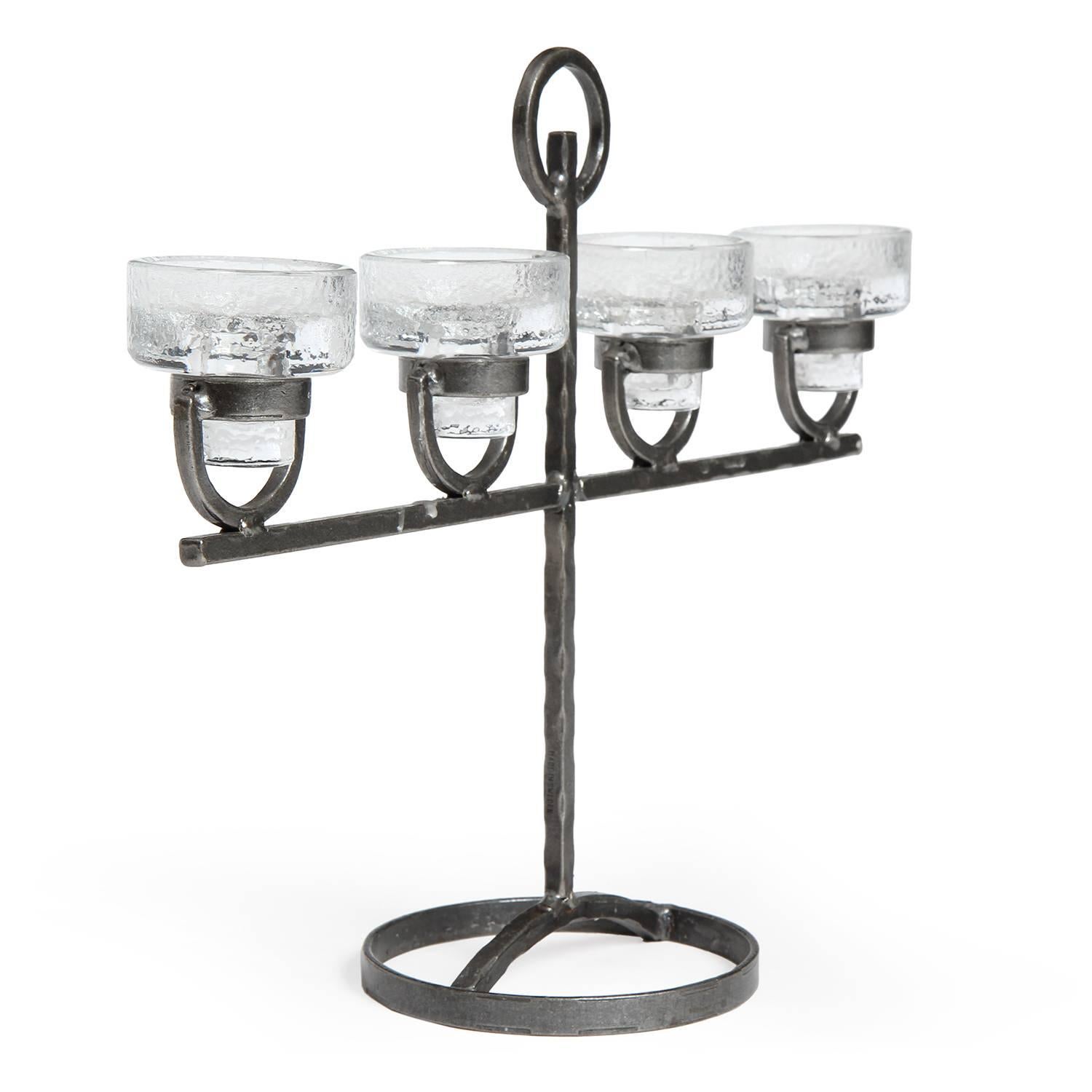 A rustic and expressive candelabra having a hand forged iron frame supporting four cast textured glass candle holders. 