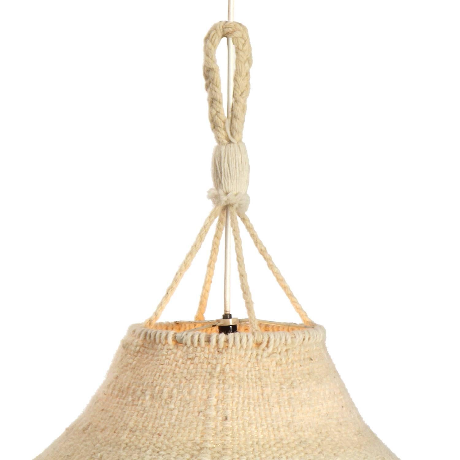 A unique and expressive artist-made handwoven and braided natural fiber hanging lamp having a tall columnar form.