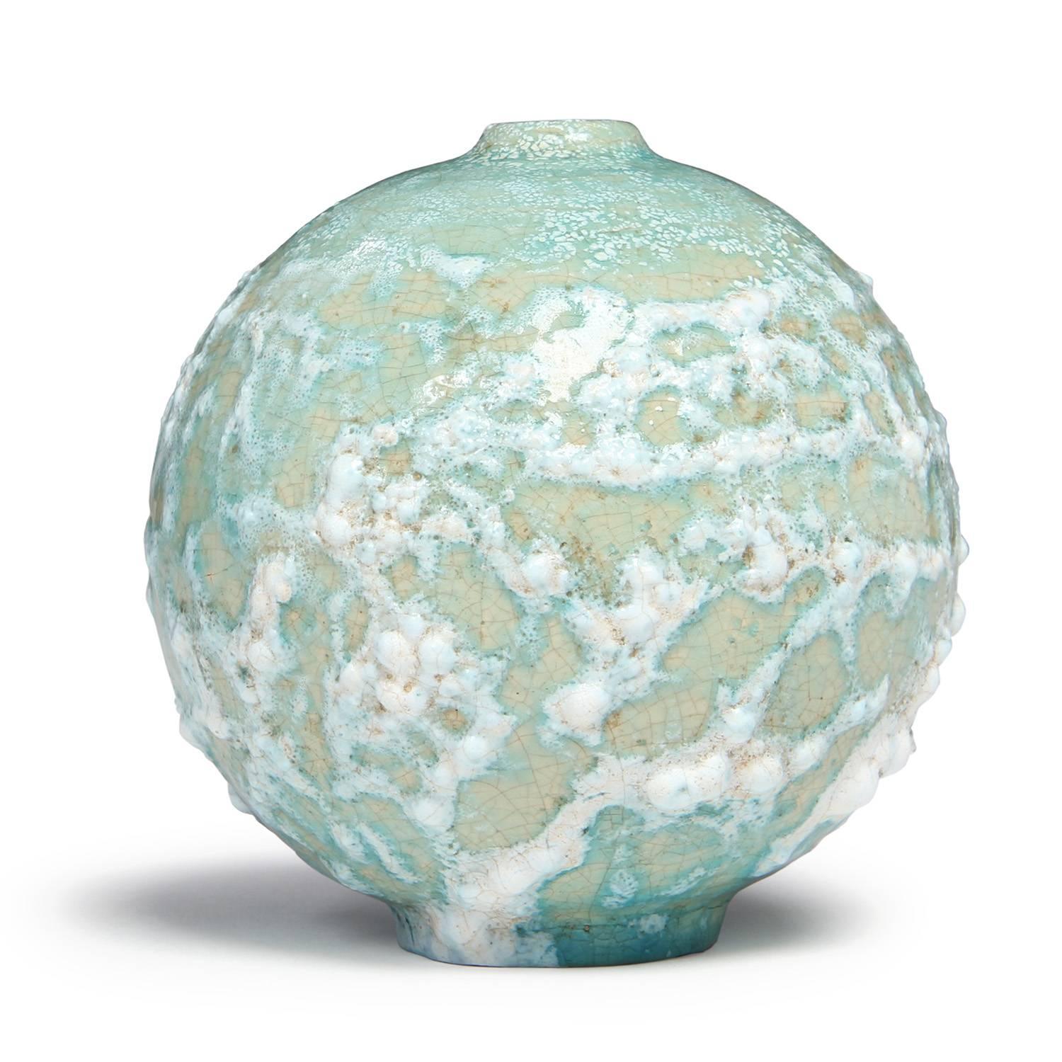 A round studio-made unique ceramic vessel with a raised narrow opening, the form covered with a rich, complex and thickened glaze in tones of celadon, cream and wheat.