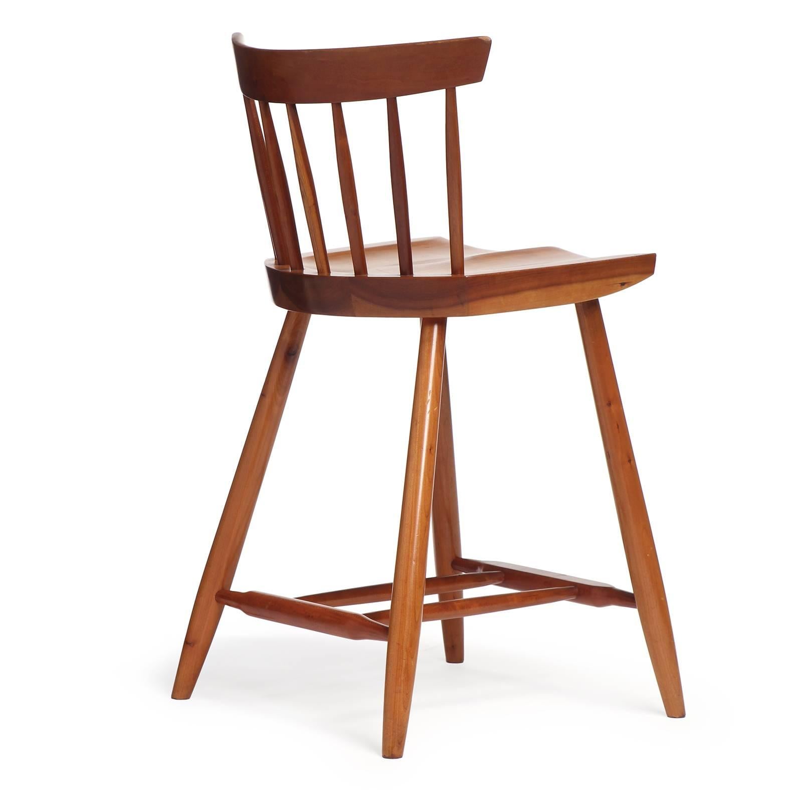 A cherry wood barstool having hand-hewn spindles supporting a curved backrest. The shaped shaped seat floats on four tapered dowel legs with a footrest stretcher.