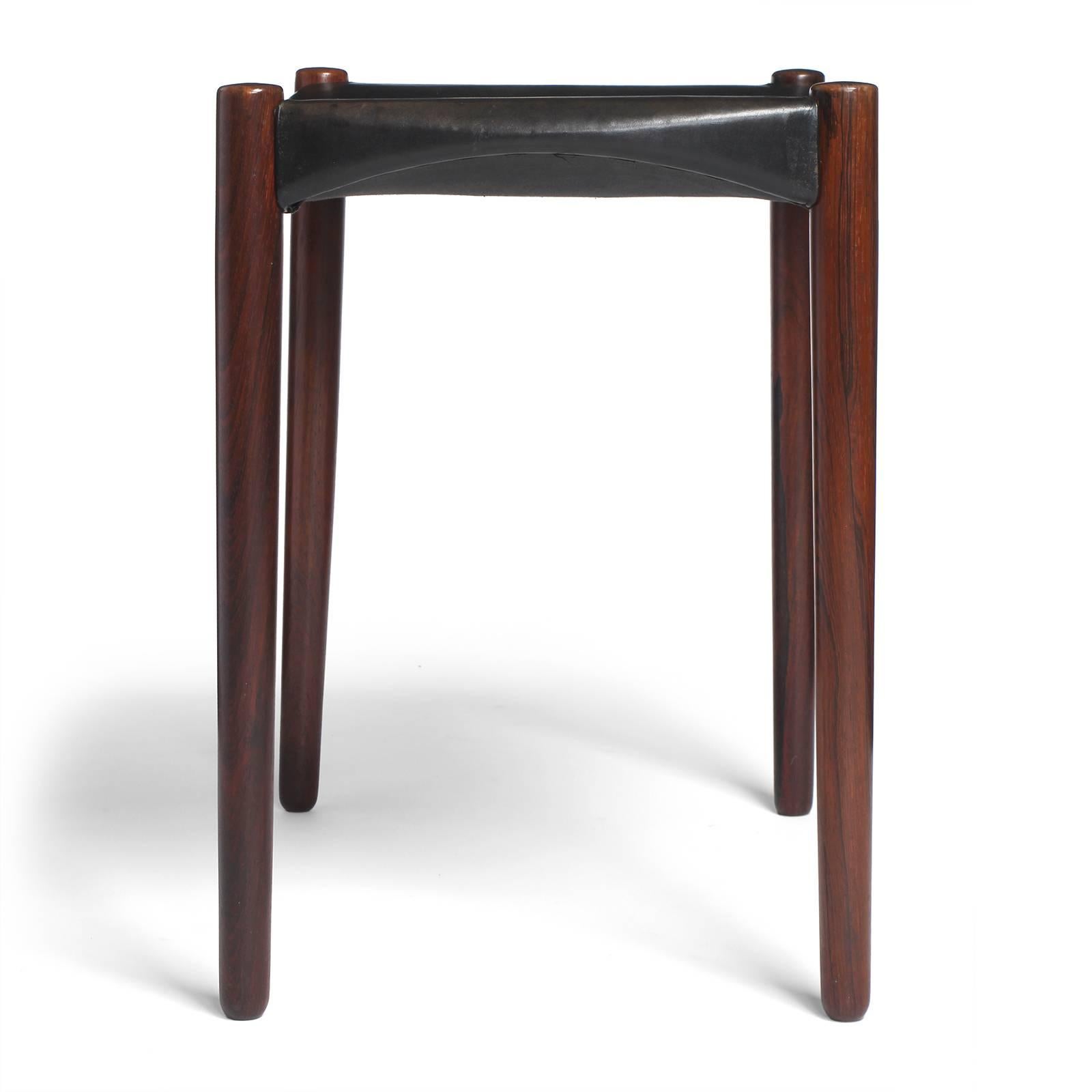 A spare and well crafted stool having a shapely black leather seat floating on tapered teak dowel legs. 
