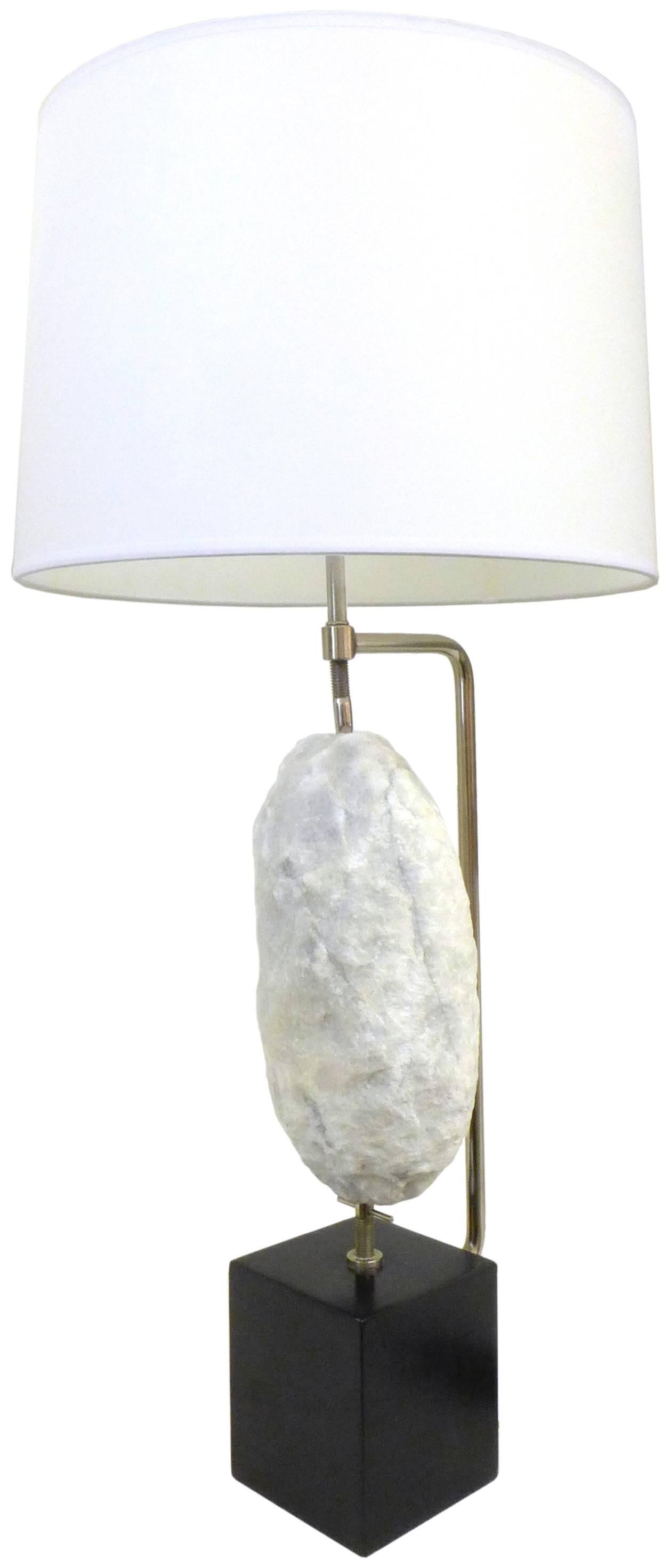 A wonderful quartz-specimen table lamp. A subtly-scintillant, rough-hewn hunk of white quartz displayed suspended in a threaded, chromed-steel, vise-like armature; all mounted to a simple black-cube metal base. An eye-catching mix of materials;