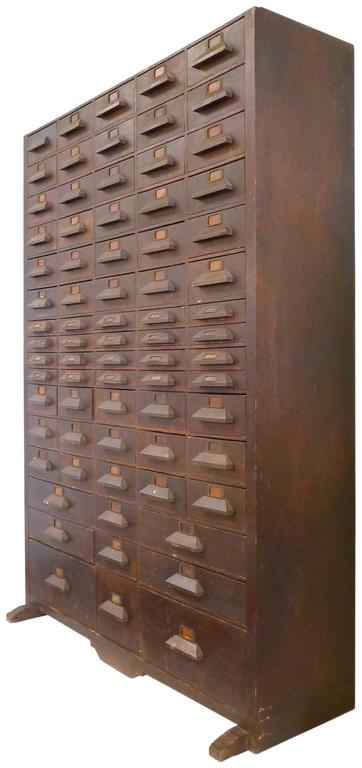 An incredibly monumental multi-drawer cabinet. Towering at over 6' tall, a facade of thoughtfully-laid-out, assorted-sized drawers with geometric, carved-wood pulls and original label-holders. A wonderful and much-desired dark-walnut patina
