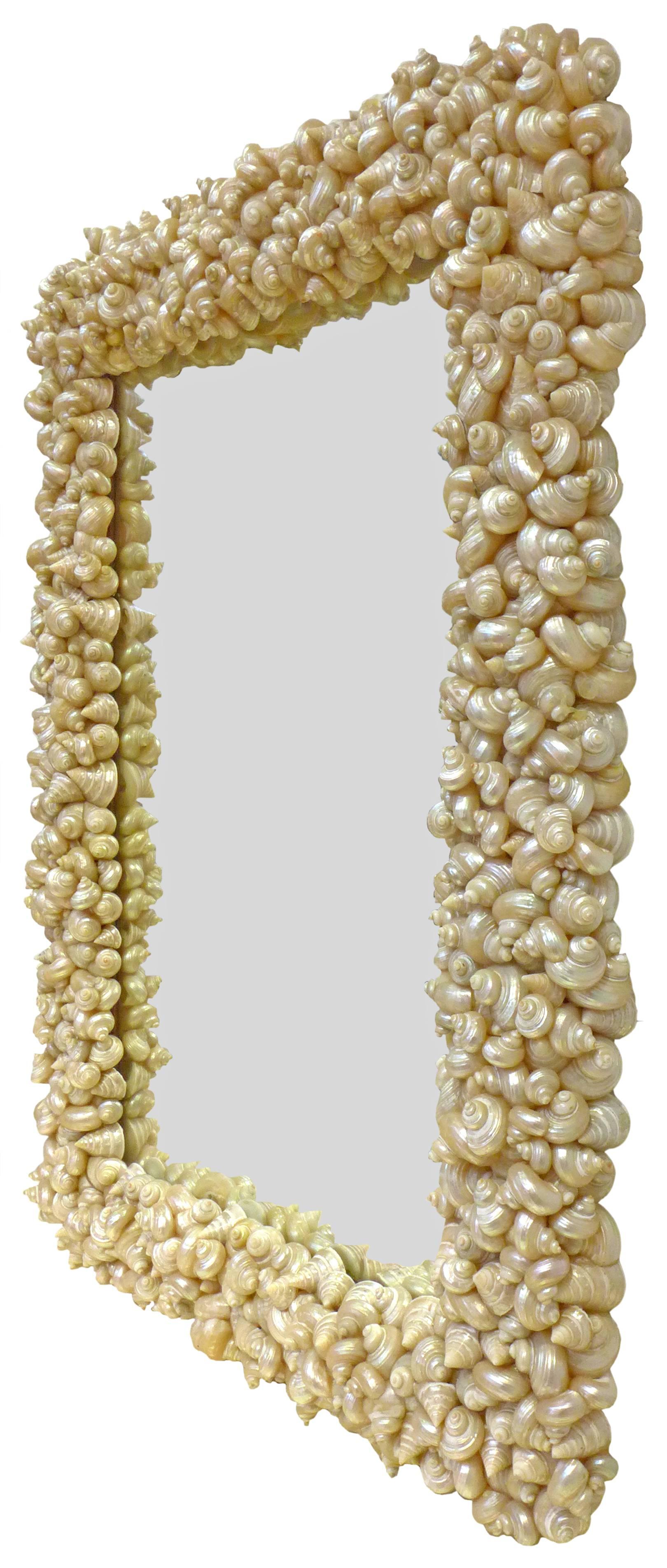 A fantastic half-length mirror wearing a frame fully encrusted with seashells. An otherwise straightforward, utilitarian item taken to an unexpected place with its meticulous and thoroughly executed, opalescent, exoskeletal perimeter. A wonderfully