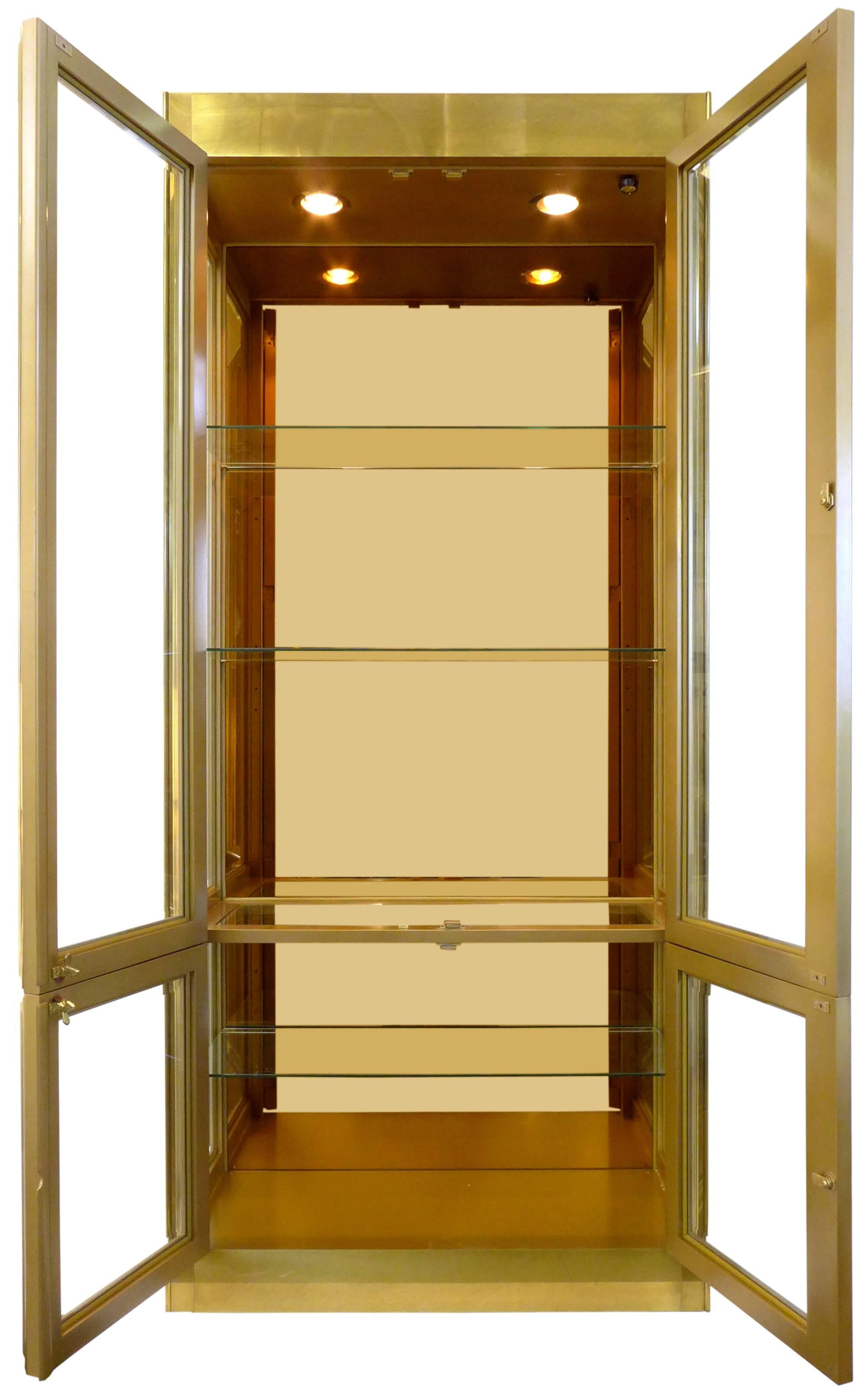 A large and impressive, brass-clad display case by Mastercraft. A striking, monolithic form elegant in every detail: Adjustable glass shelves, mirrored back, two dimmer-switched overhead lights and graceful frame details on the door-fronts. In
