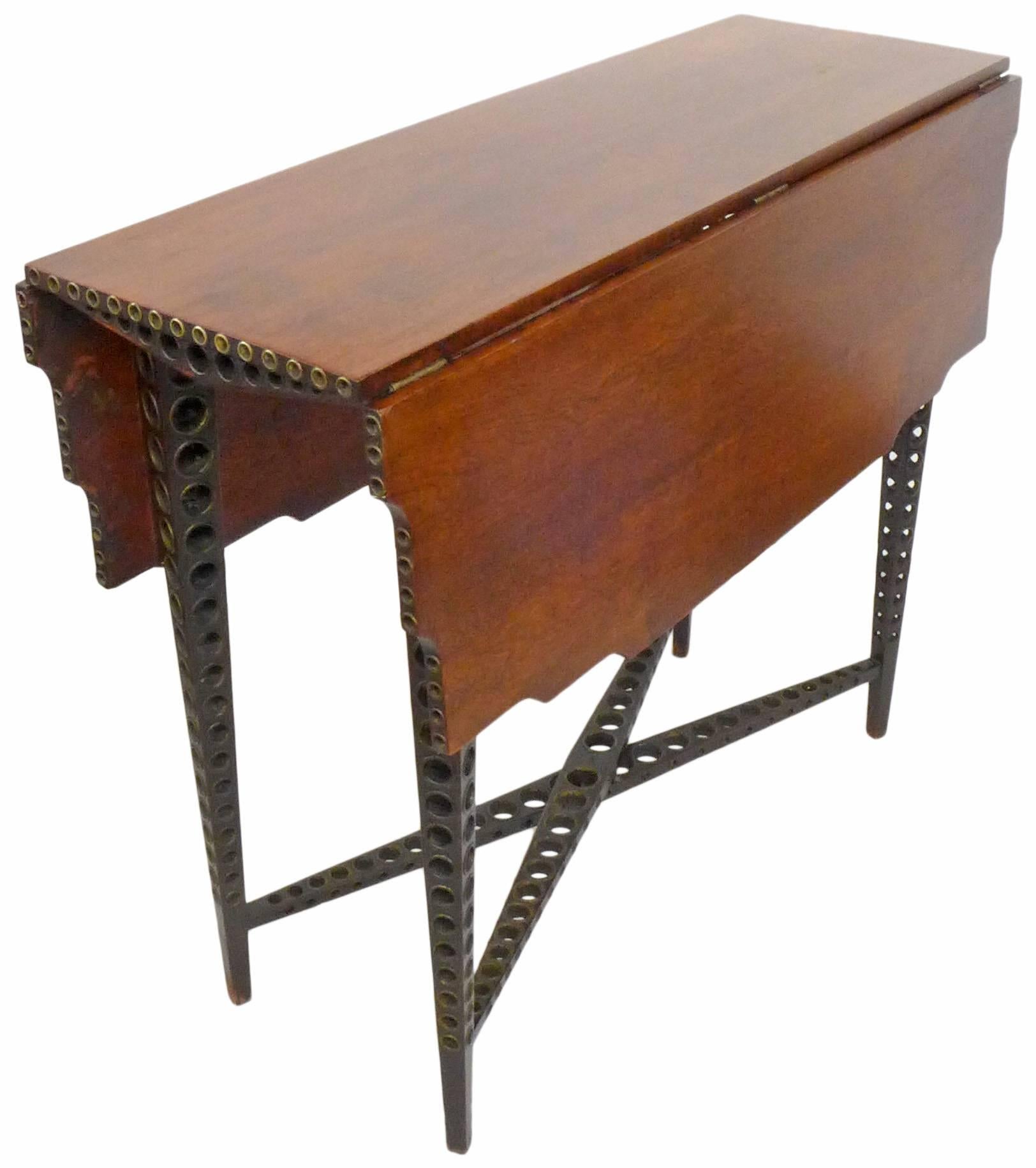 A wonderful and extremely unusual early 20th century drop-leaf table. Multi-directionally perforated, elegantly tapered legs and cross stretchers with graduated circles and brass grommet details. A gently scalloped top detail and additional