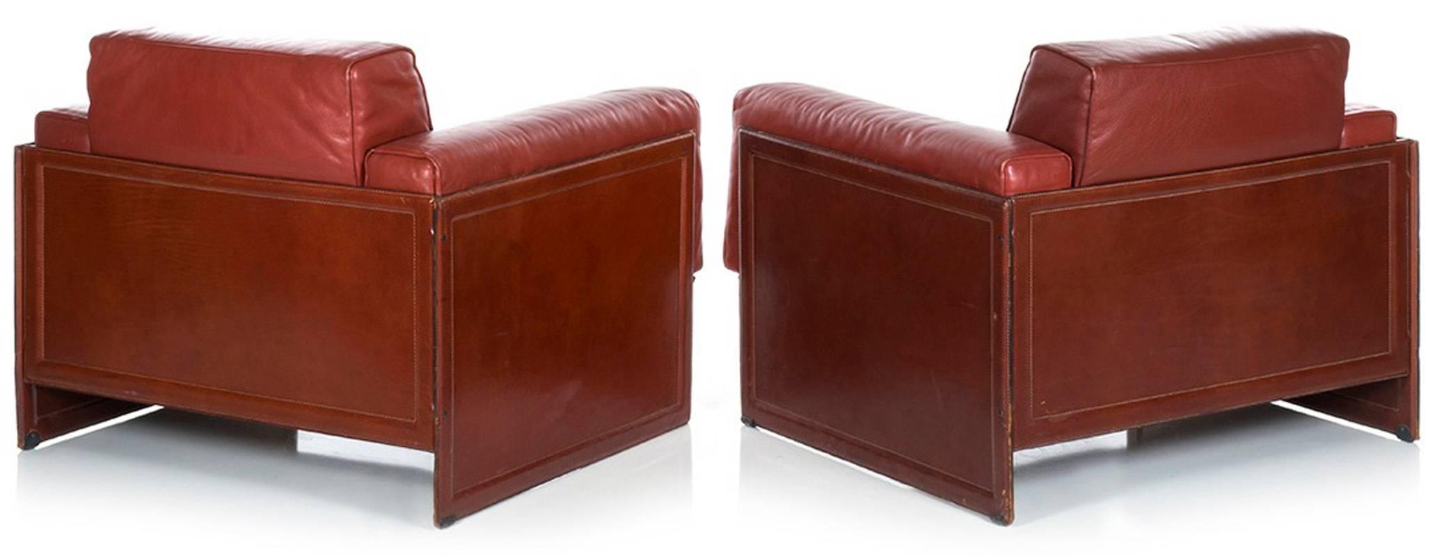 A fantastic pair of all original Korium KM3/1 club chairs by Tito Agnoli for Matteo Grassi. Perfect examples of 1970s Italian design: clad entirely in thick, high-quality, rosso bulgaro leather; decoratively frame-stitched side panels support four