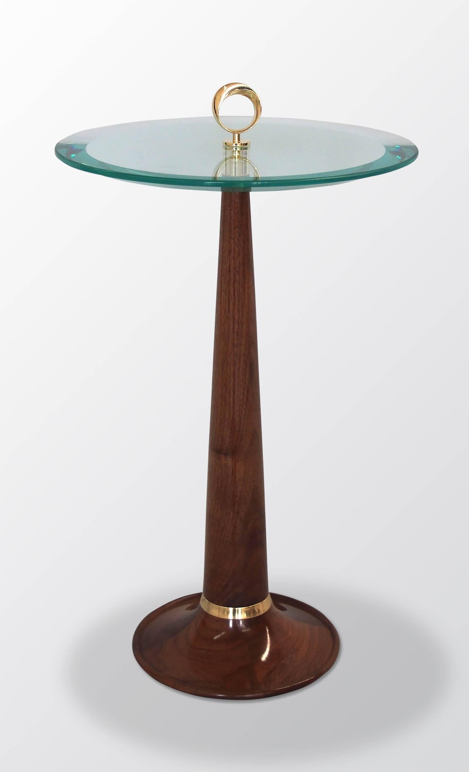 A very petite occasional table in solid carved walnut with an acute bevelled glass top, original Moebius-strip design brass hardware. French polish finish.