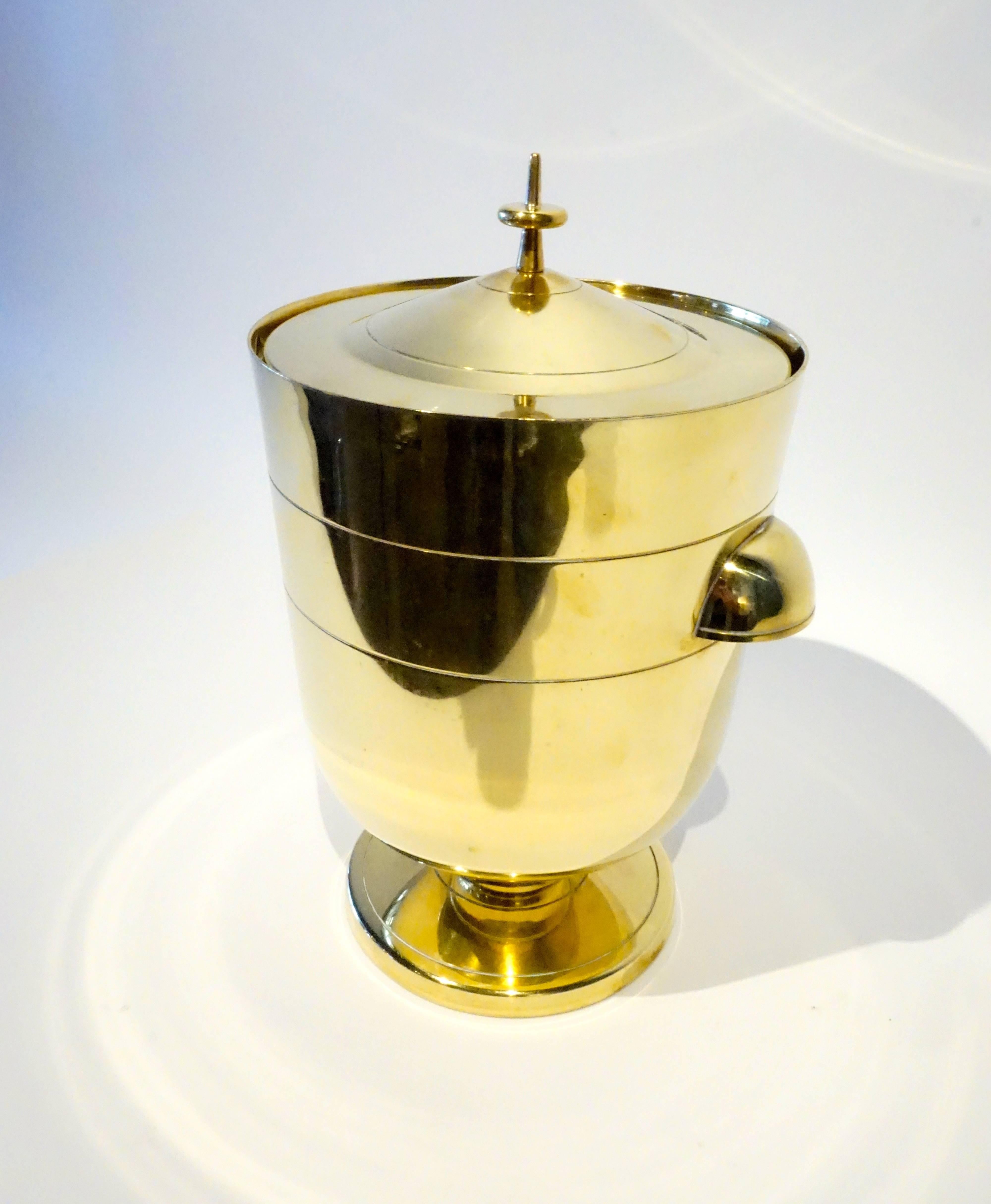 A stylish and highly sought after polished brass ice bucket or wine cooler designed by Tommi Parzinger and made/retailed by Dorlyn Silversmiths in the 1950's. The bucket retains its original mercury glass lined interior that is acid-etched with