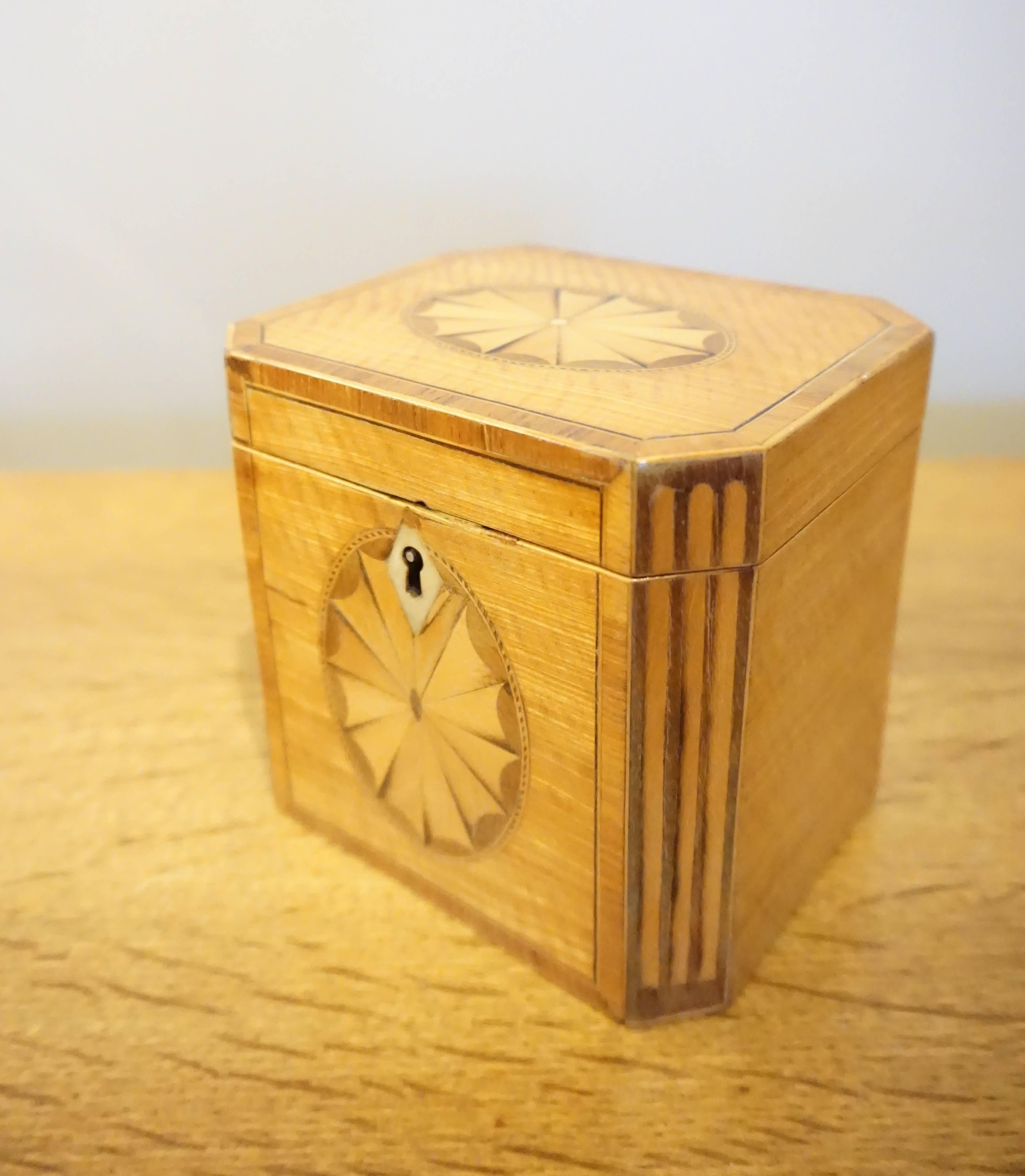 An English George III period inlaid satinwood octagonal tea caddy. Circa 1800. The top and front surfaces of the box are decorated with fan motifs set into oval frameworks and the edges are cross banded with rosewood and inlaid ebony. The canted