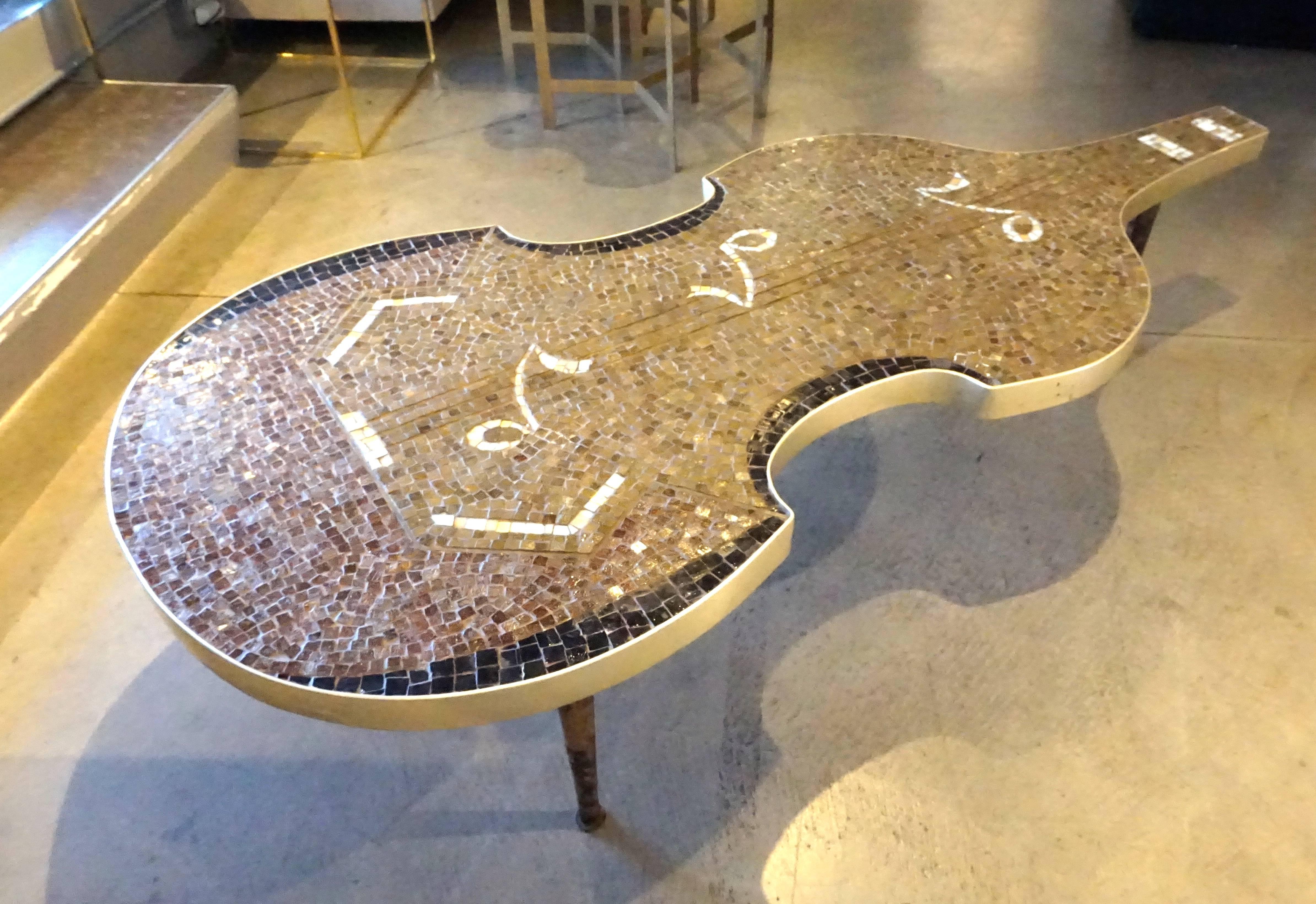 A whimsical glass mosaic top coffee table in the form a of a Cello from the 1960s. The intricate top of the table is banded with brass and is detailed with musical notes. The legs are solid brass and were once painted black. The mosaic tiles are