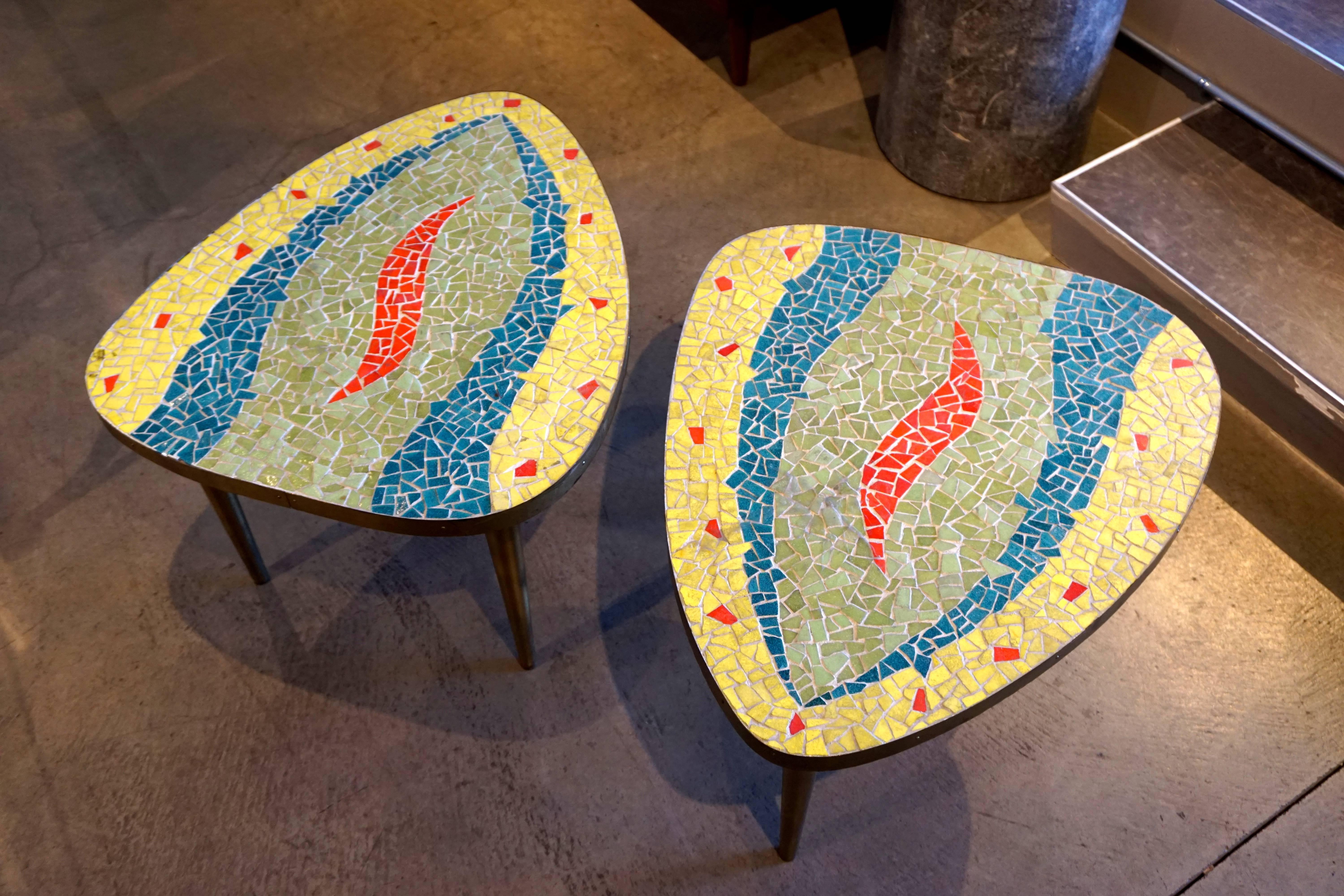 A pair of glass mosaic-topped occasional tables from the 1960s. The tables are shaped like guitar pics and the mosaic tops are contained with a thin band of brass. The legs are wood that has been painted gold. Sold only as a pair.