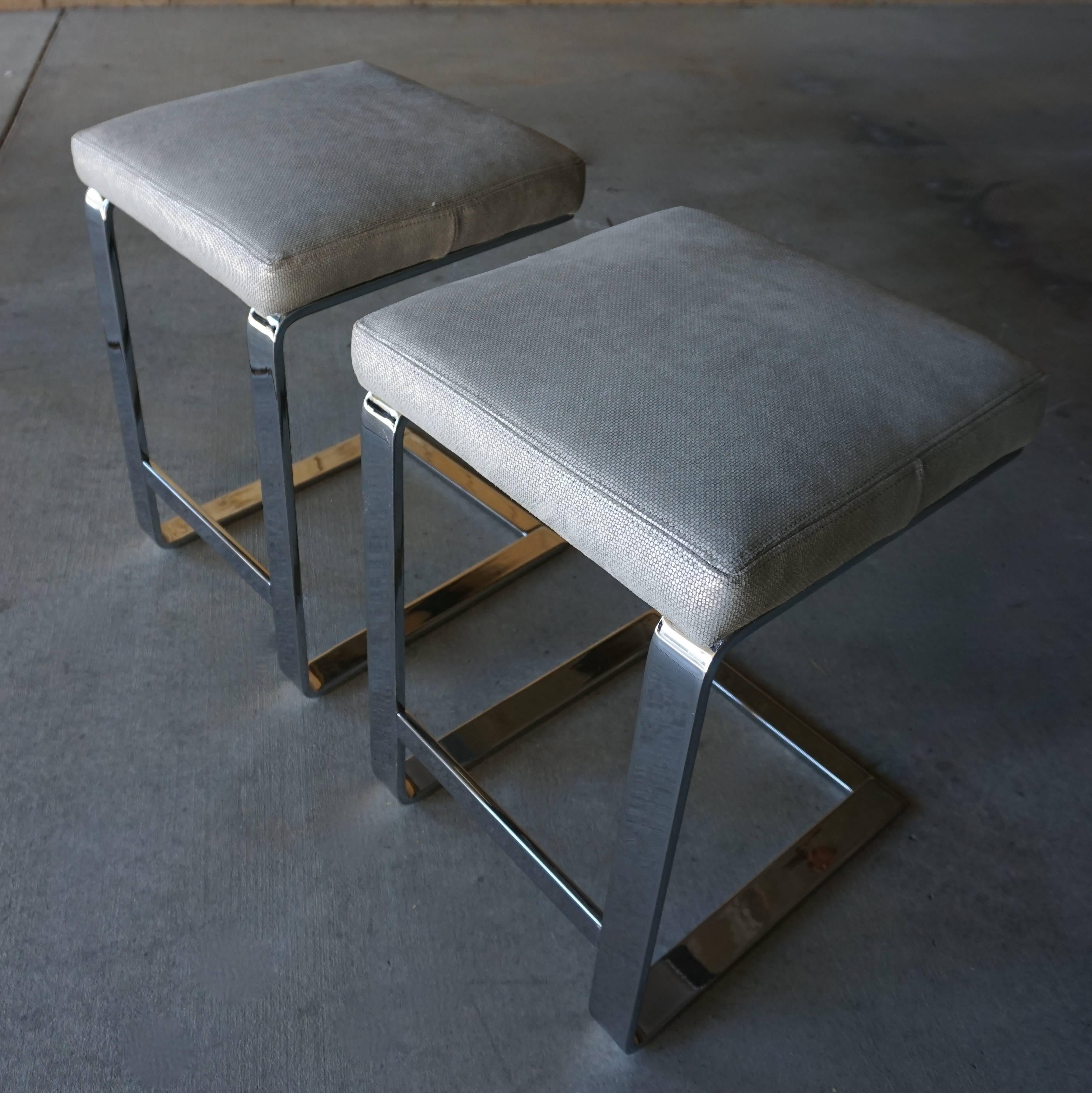 A pair of nickel plated steel counter height stools attributed to Leon Rosen for Pace in the 1970s. The bases are a combination of solid and hollow flat bar steel and the seat are newly reupholstered in a soft and textured silver leather. The