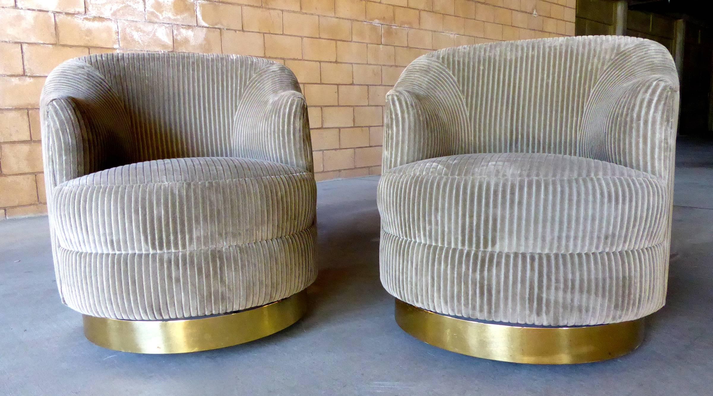 A pair of circular club chairs with brass plated metal bases, designed by Karl Springer and made in the 1970s. The chairs have casters underneath the bases and move easily. They have been recently upholstered in a tan/coffee-colored wide wale