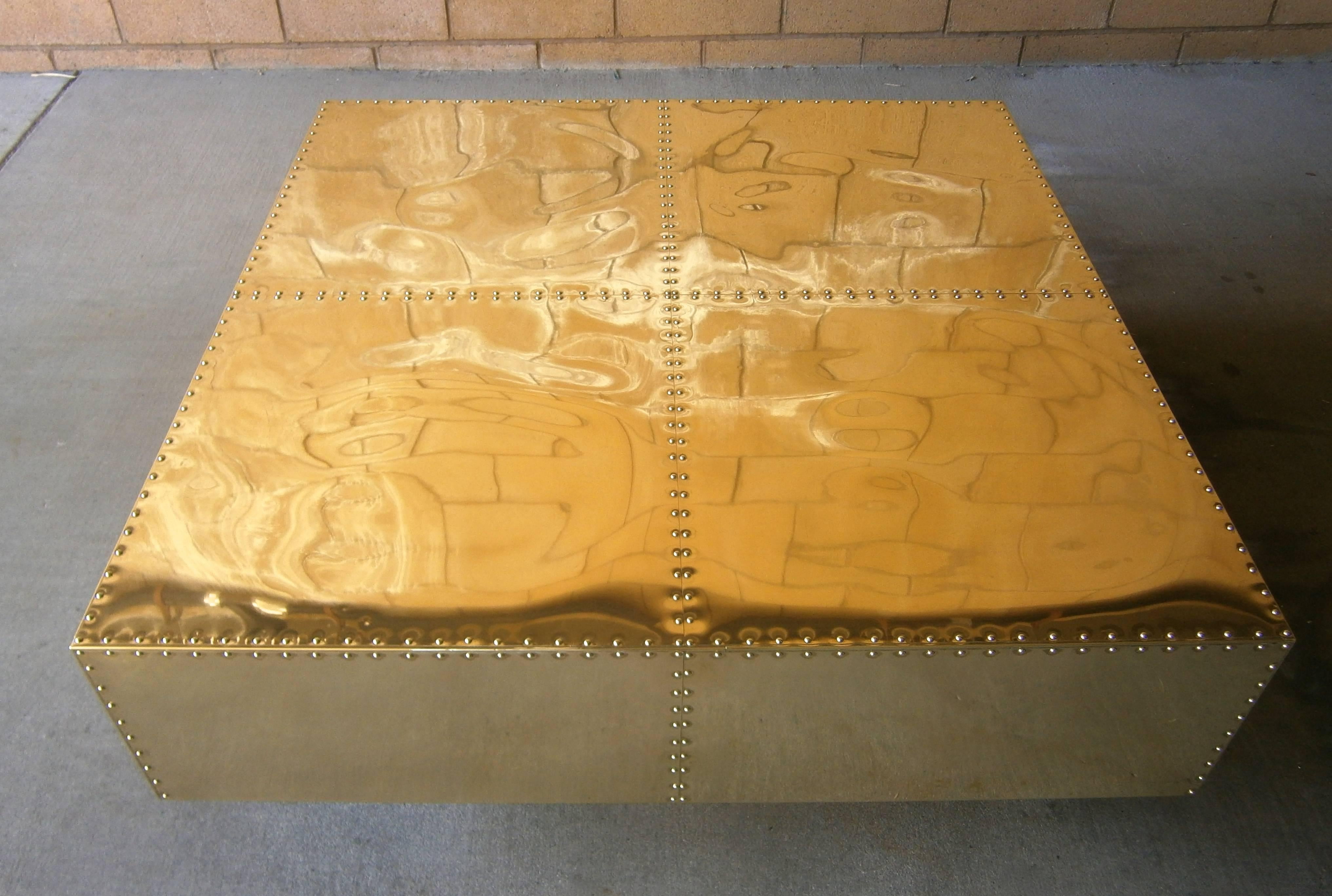A gleaming brass-clad square coffee table made by the Spanish manufacturer Sarreid Ltd. in the 1970s.  The top is studded and separated into four segments and floats above a recessed plinth base. The table has recently been professionally polished