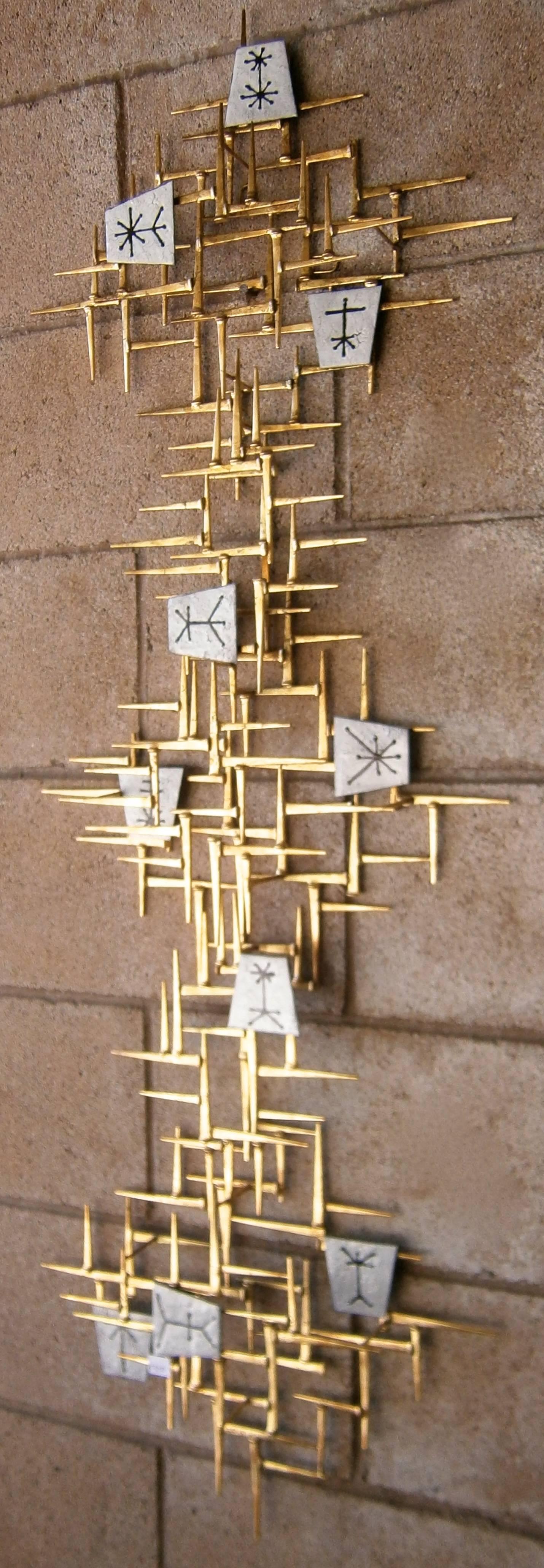 A contemporary gilded metal wall sculpture with hand-made enamel details made by American artists Del and Brenda Williams. The asymmetrical lay-out of the sculpture, along with the black and white enamel plaques give the piece an amazing Mid-Century