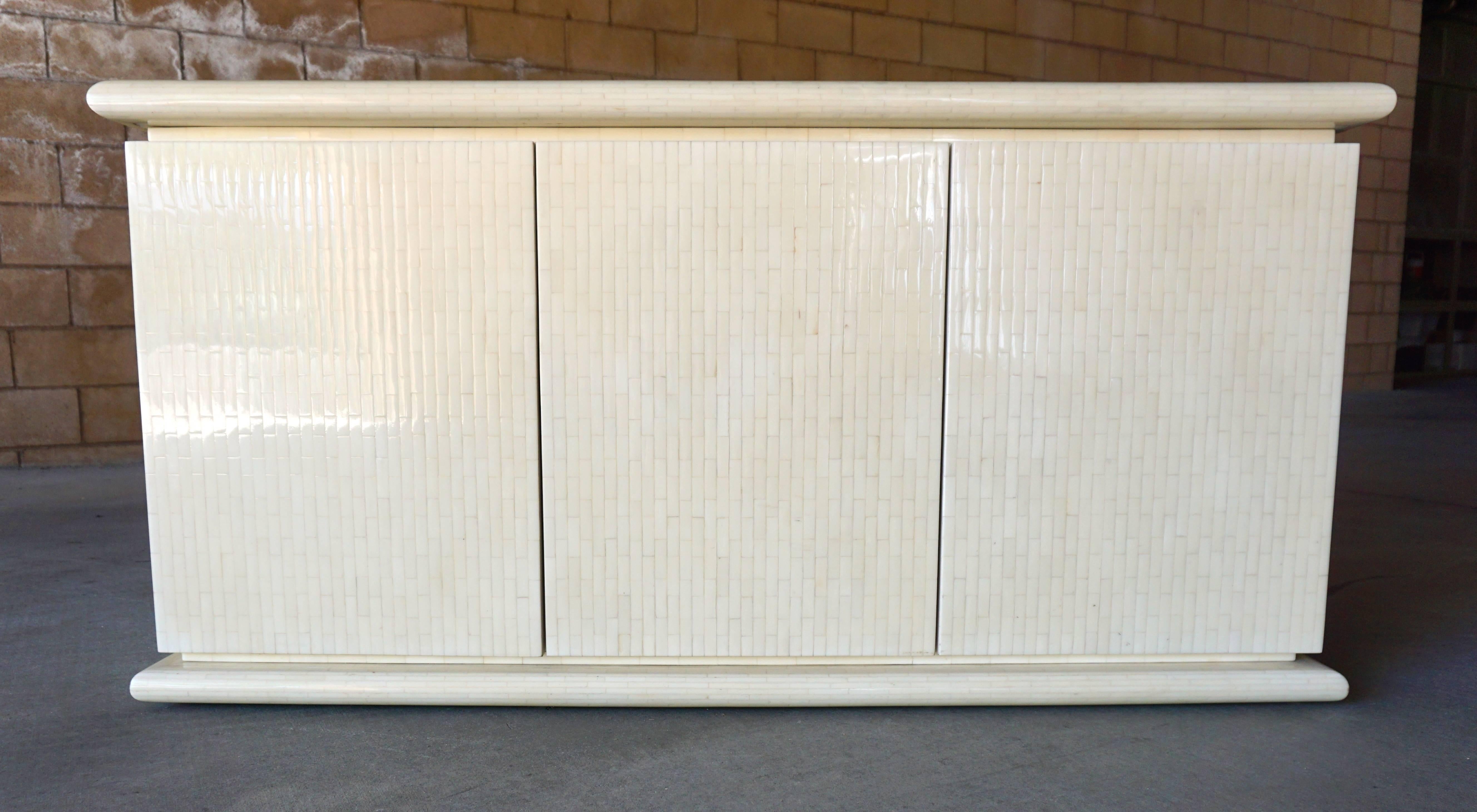 A tessellated bone three-door credenza / cabinet from the 1970s, attributed to Columbian designer and manufacturer Enrique Garcel. One of the three sections houses a set of 4 drawers with the others having adjustable shelving. The chic styling and