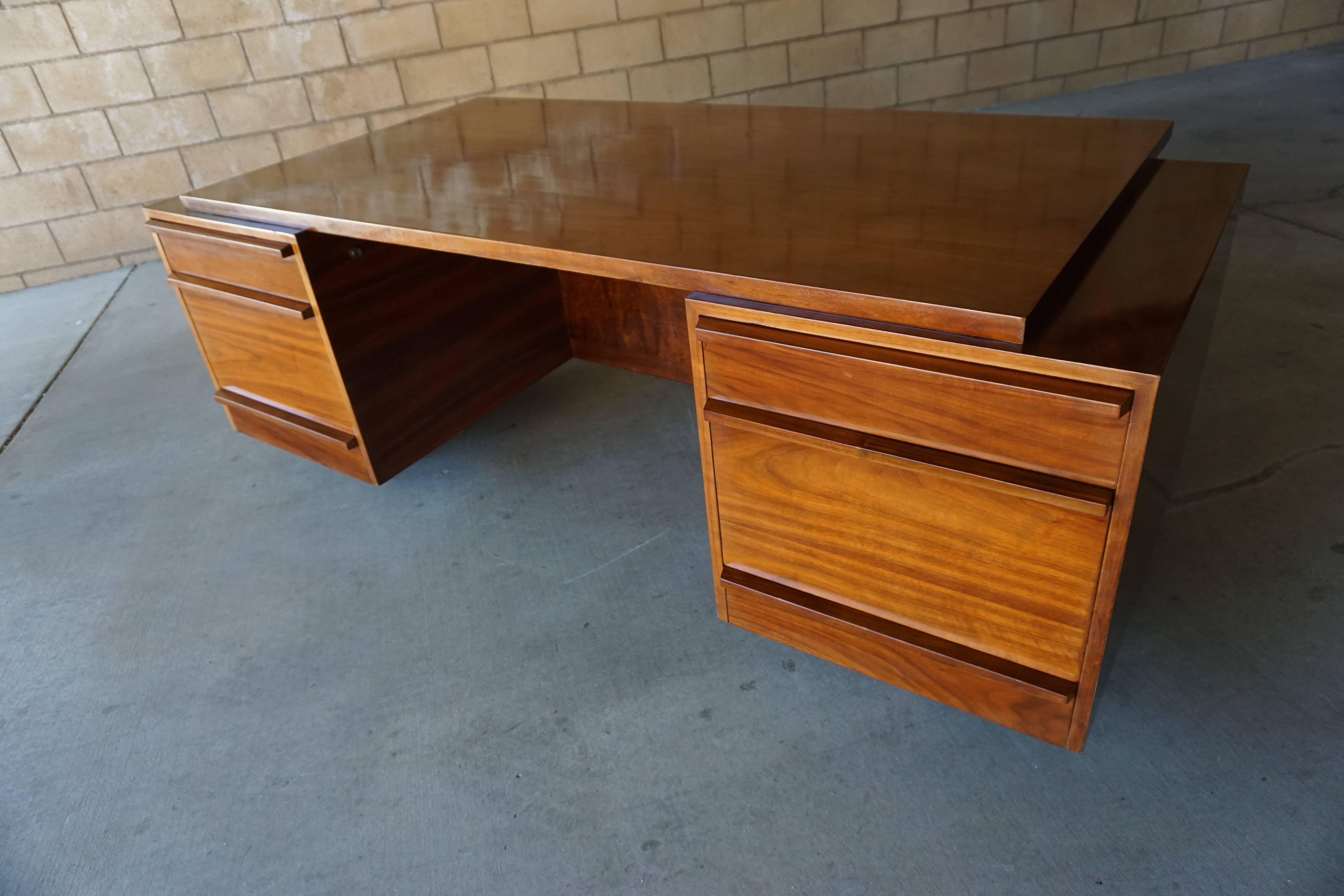 A large and impressive custom-made executive desk from the 1950s. 
A pair of generously proportioned banks of drawers support a large and functional work surface that steps back at the sides and slightly cantilevers over the front. The desk was