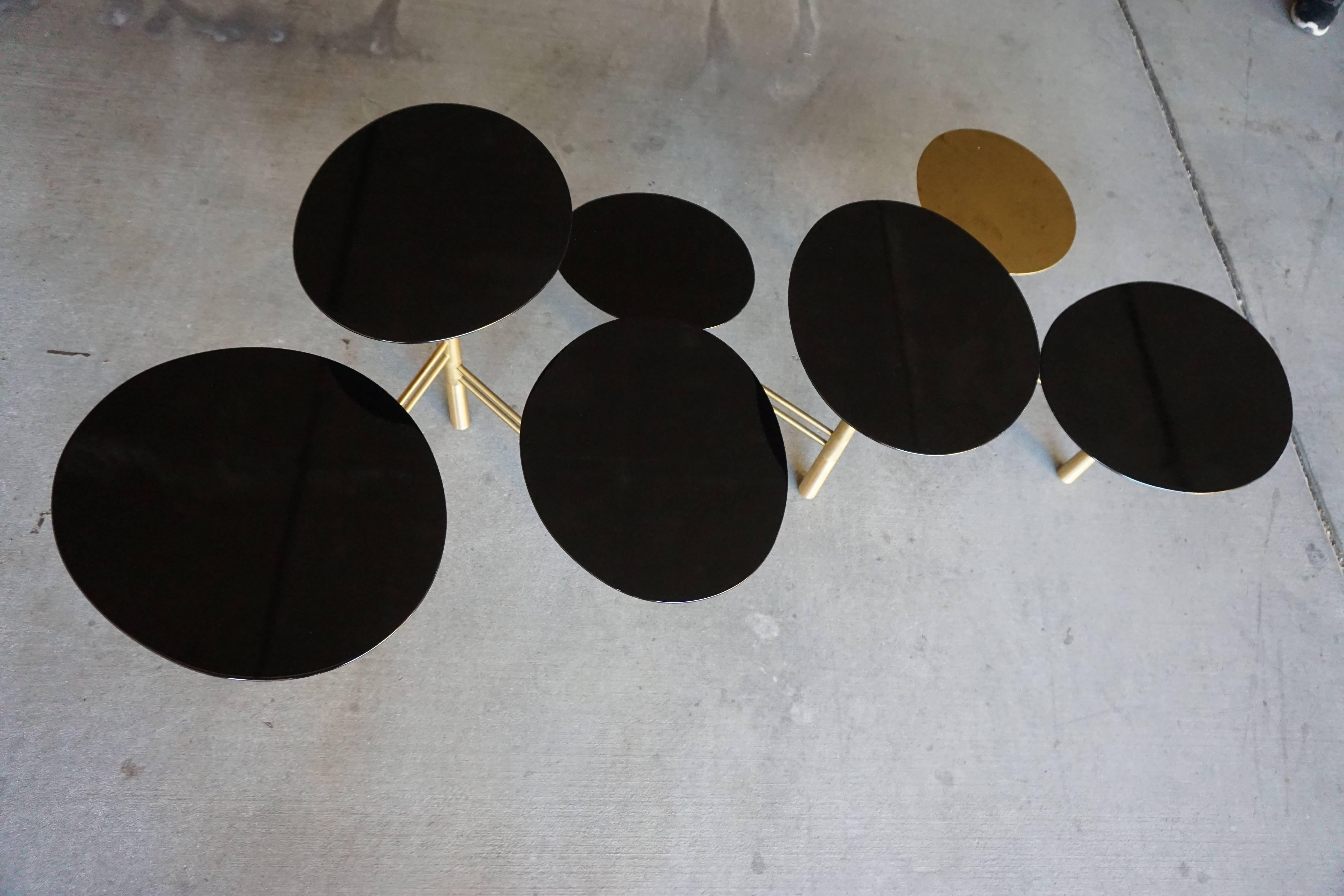 The pebble table is a contemporary brass and black lacquered multi-tiered low table by Lebanese furniture designer Nada Debs. The table has a brushed brass articulated base with six black lacquered "pebble" tops and one brass