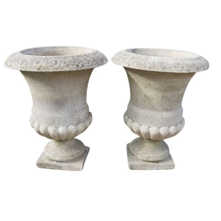 Made circa 1940 this pair of stone urns has been well cared for. Cast in the traditional urn style with an overturned bell shape giving way to a tapered support brace atop the plinth. Monumentally sized urns of this style have been found in