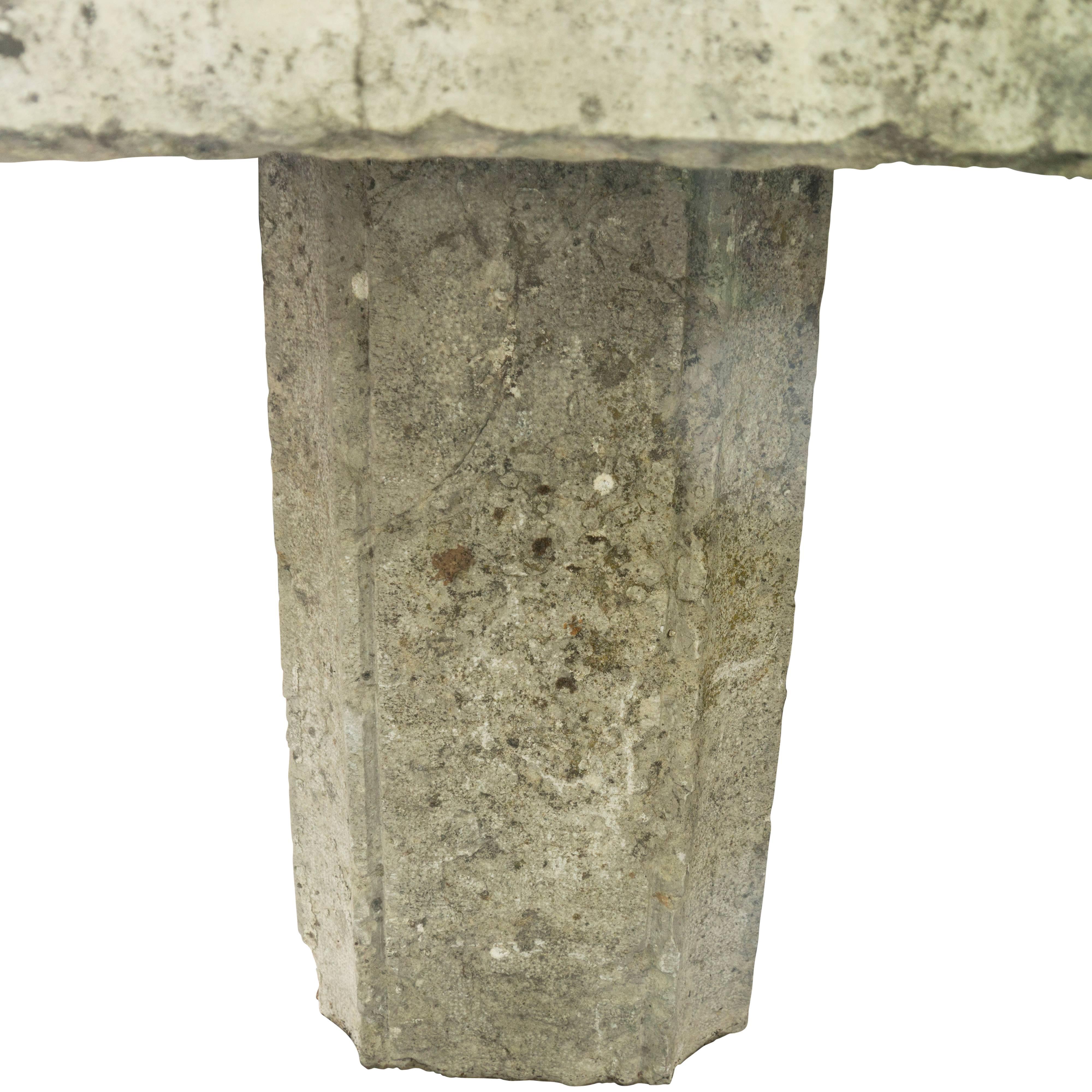 A monumental antique stone garden table, comprised of a massive flattened stone slab table top balanced on a thick pedestal leg. It stands 30 inches tall, which includes a four inch thick stone top and the 26 inch in height base. The base is