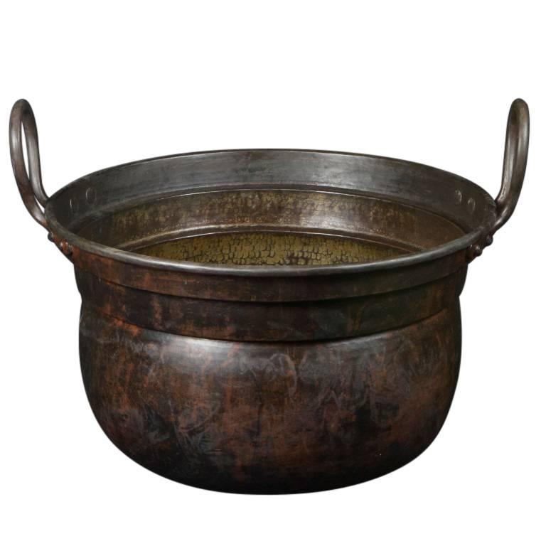 A lovely antique planter similar in shape to a cauldron, this copper vessel is 15 inches tall at the top of the looped handles and 19 inches in diameter, the bowl portion is 11.5 inches tall. The copper is an incredible brown color marbled with a