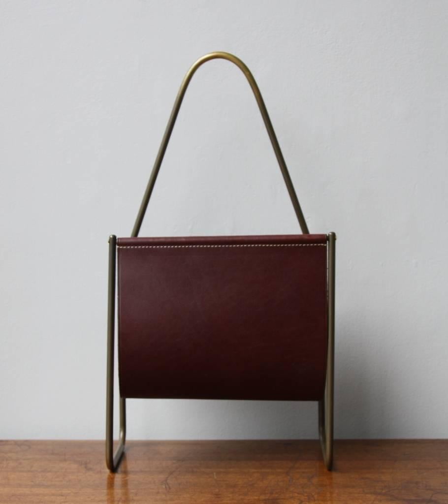 Vintage magazine stand designed and made in the Auböck Werkstatte, Vienna, circa 1960. 
The curvy frame in polished brass is covered by a uniform patina dark in colour; the leather is coloured in burgundy. 
In overall excellent condition.