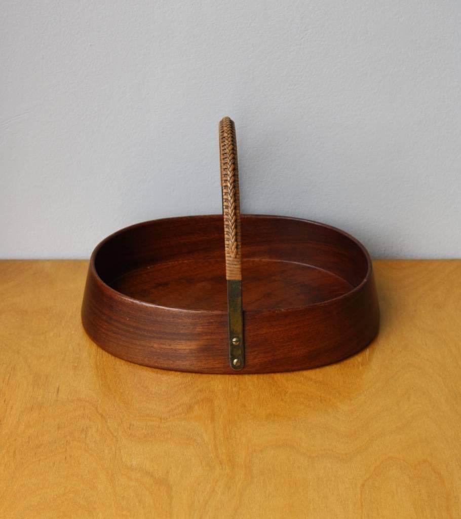 Handled bowl designed and made by Carl Aubo2ck III, Vienna, Austria, 1960s.
The body is made of carved mahogany, an arched brass handle is partially covered in handwoven wicker and attached to the wood with four brass screws.
The design is