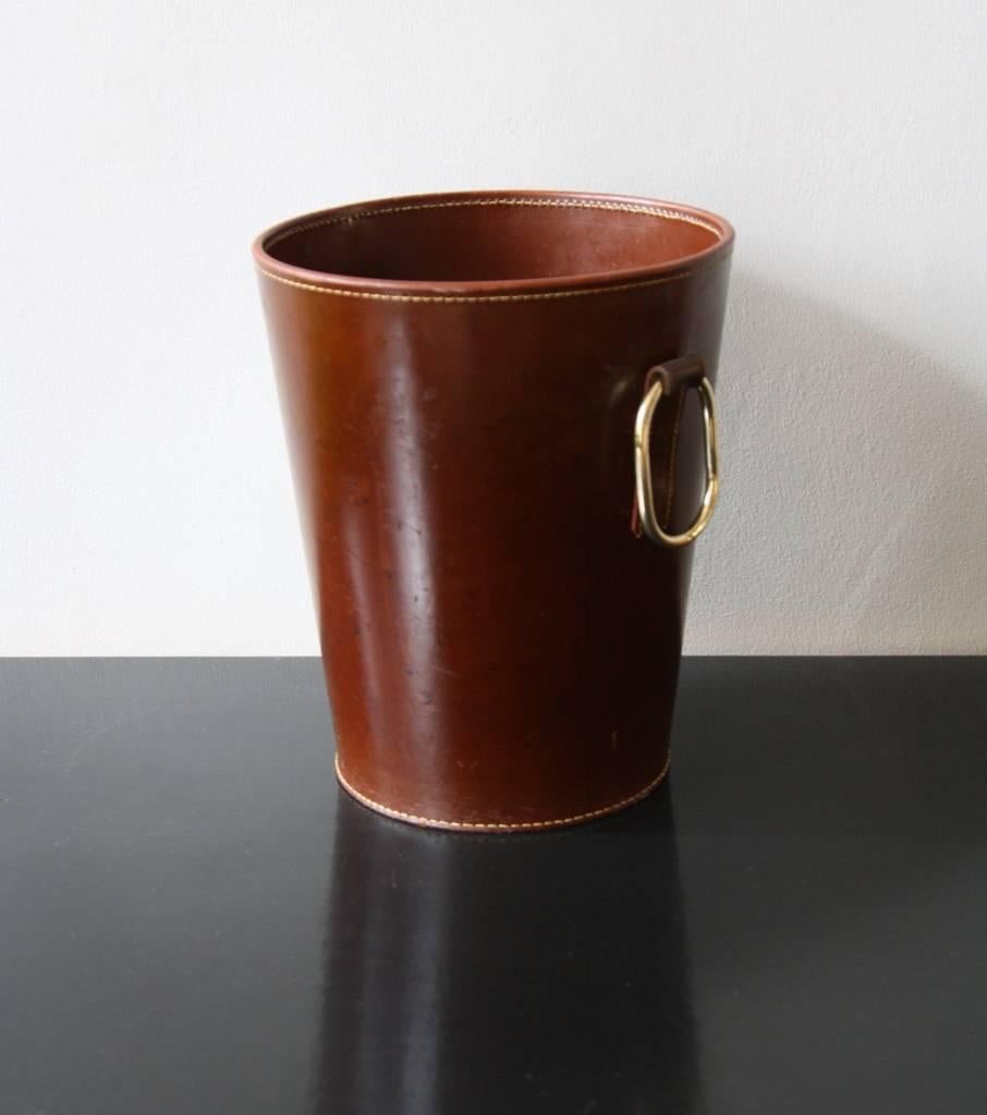 Vintage paper basket, Vienna, 1950s. Made out of leather of a dark brown colour, it is sewn up with white stitching and has a sculptural handle in polished brass. 
In overall good condition.