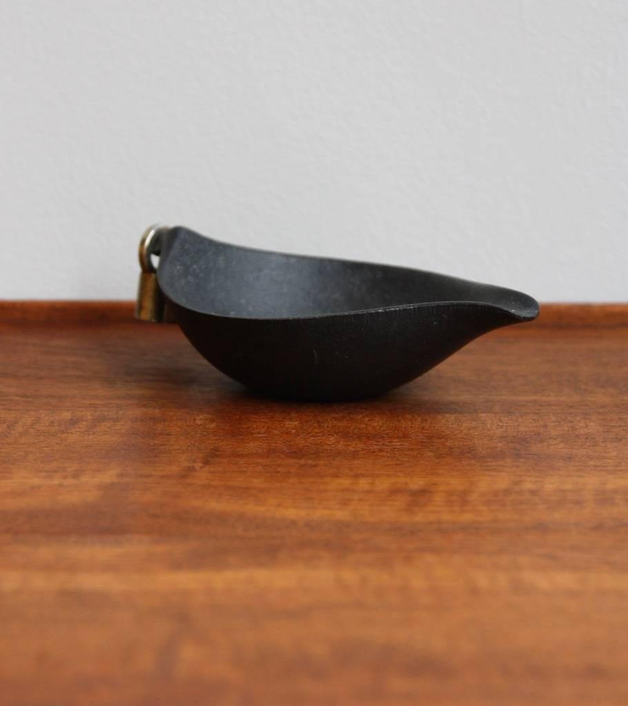 A vintage ashtray with tamper by the Auböck Werkstatte, Vienna, circa 1950.
Marked 'GG' on the underside, it is made of cast iron brass and has a key shaped tamper in nickel-plated brass; the latter hangs to one extremity of the ashtray, which, in