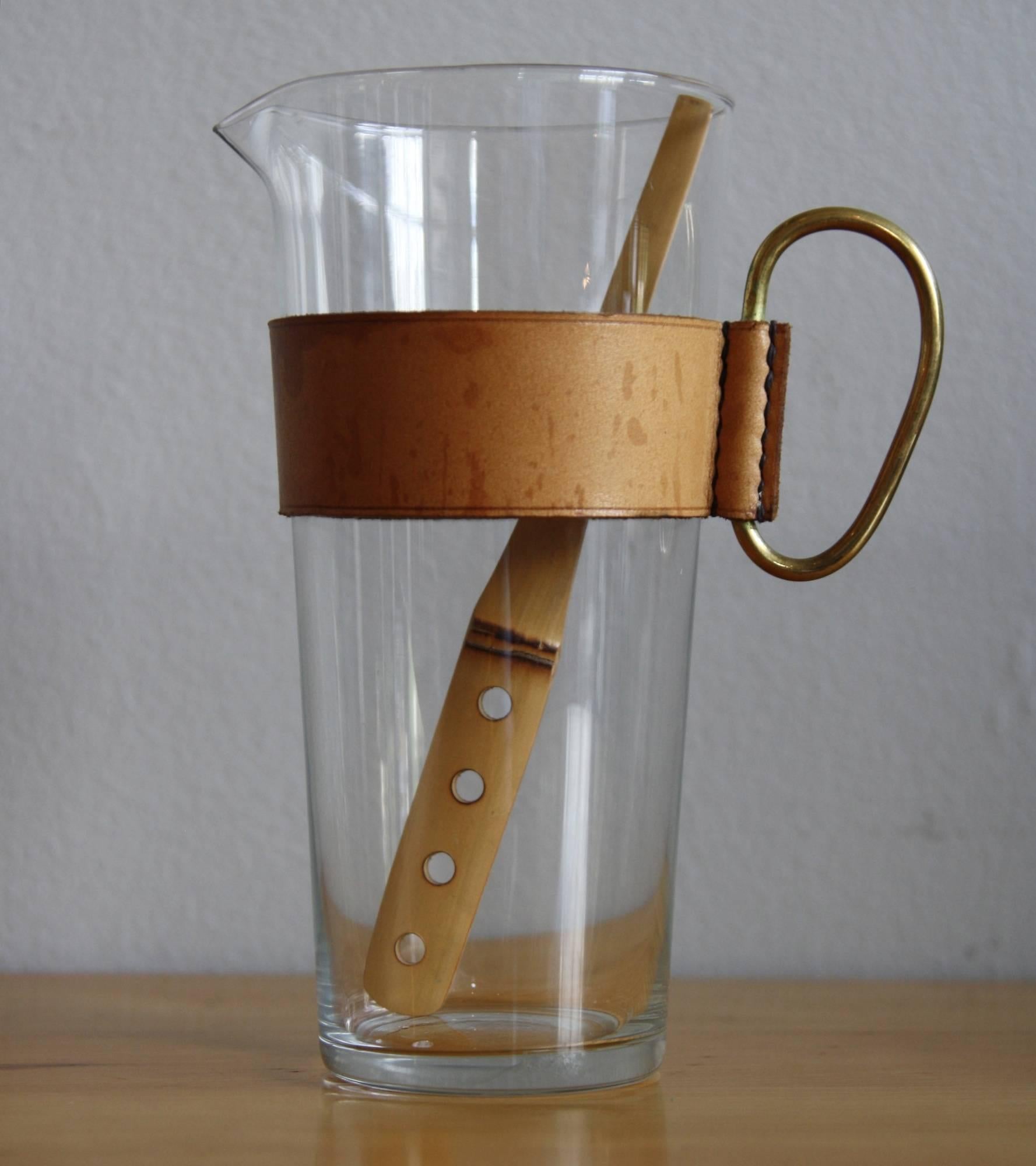A small glass pitcher with a removable handcrafted leather collar, solid brass handle and bamboo stirrer. Designed and made by Carl Auböck in Vienna.