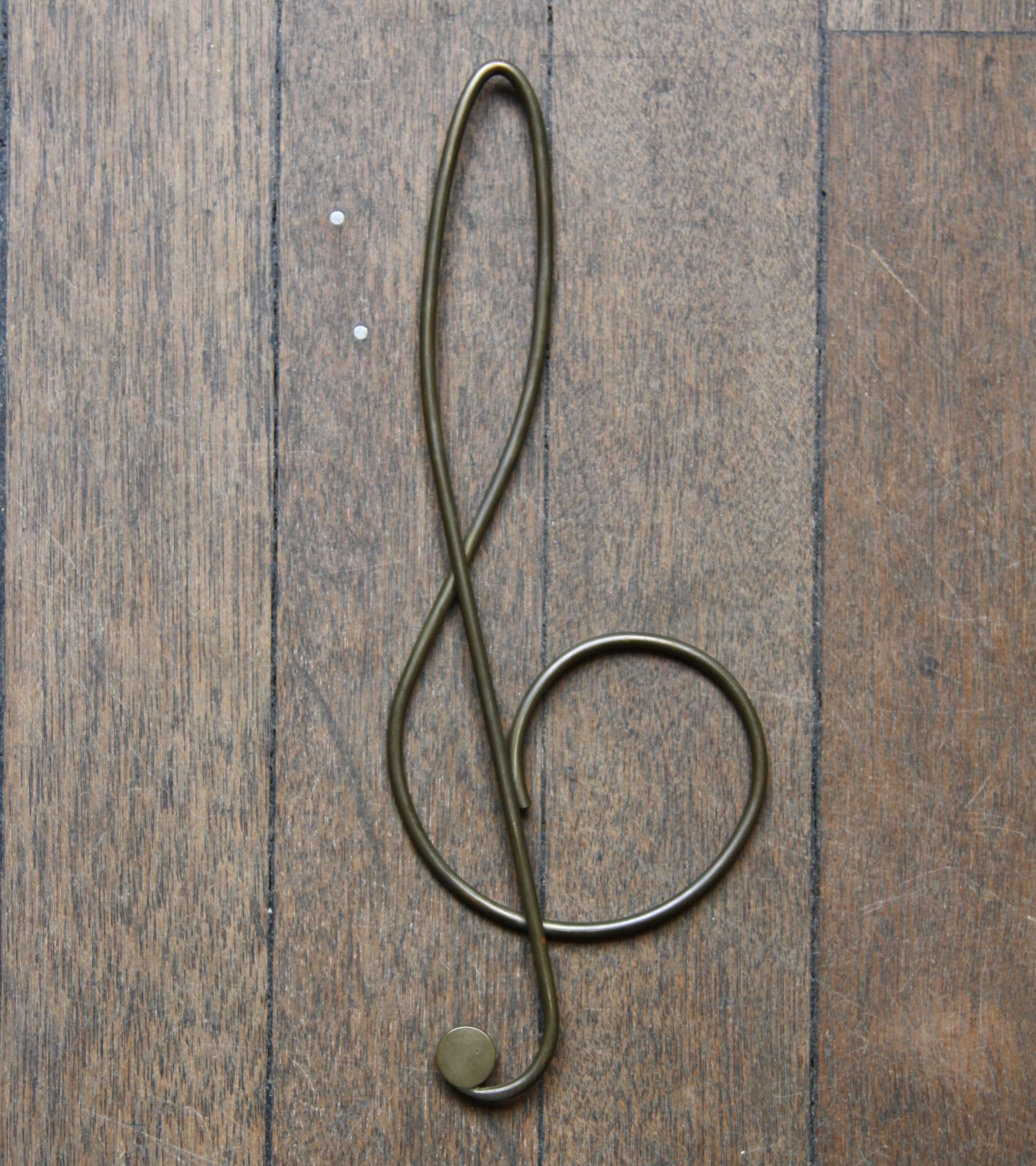 An oversized solid brass paper clip in the shape of a treble clef designed and made by Carl Auböck II, in Vienna, Austria, circa 1950.
Designed to keep documents in order the clip is formed of a continuous brass wire which overlaps in the middle to