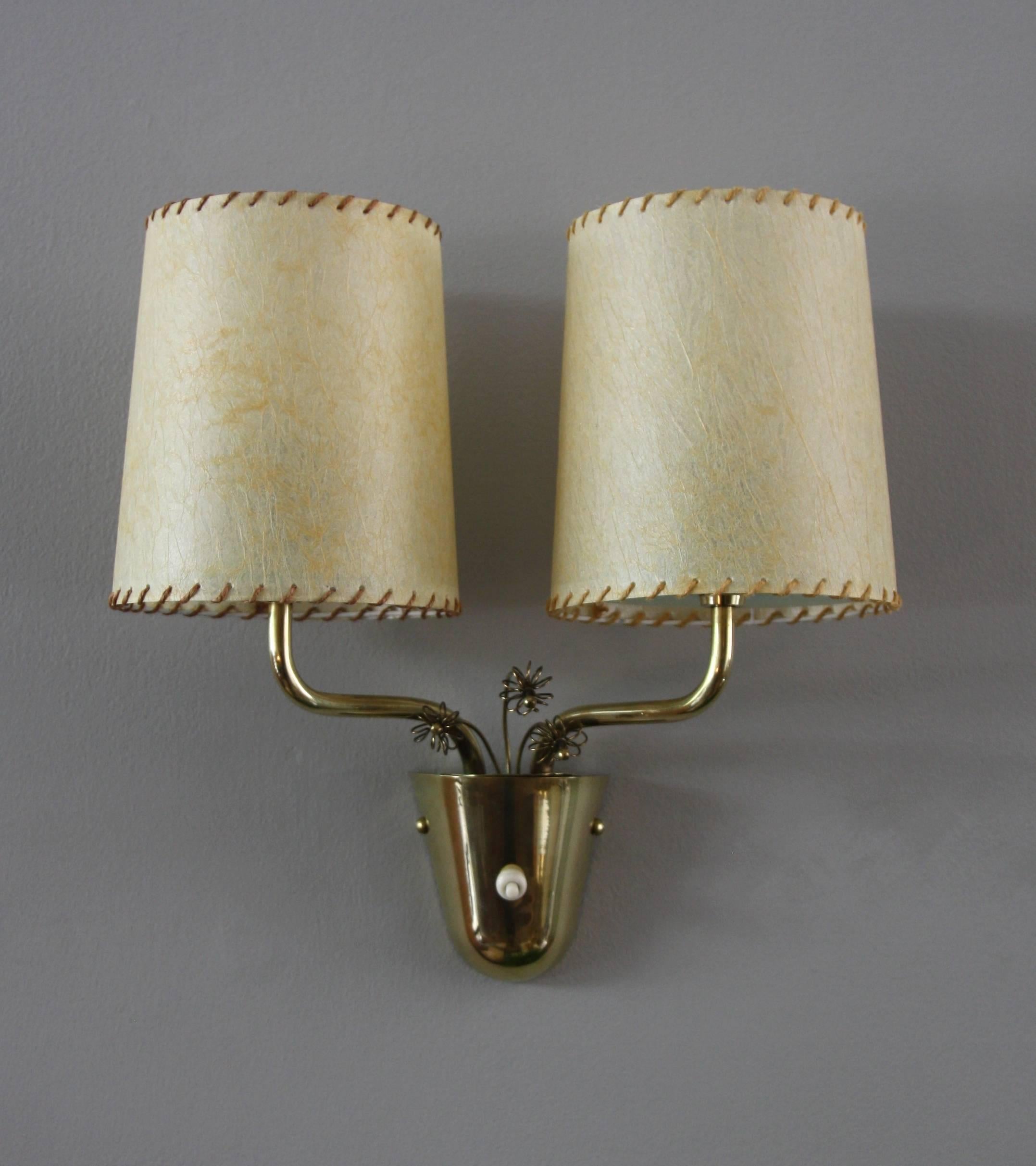 A vintage mid-20th century wall light designed by Paavo Tynell for Taito Oy, Finland. 

Made, circa 1955 the wall lamp with three delicate-looking brass flowers is a great example of Tynell's design. 

The juxtaposition of the materials used in