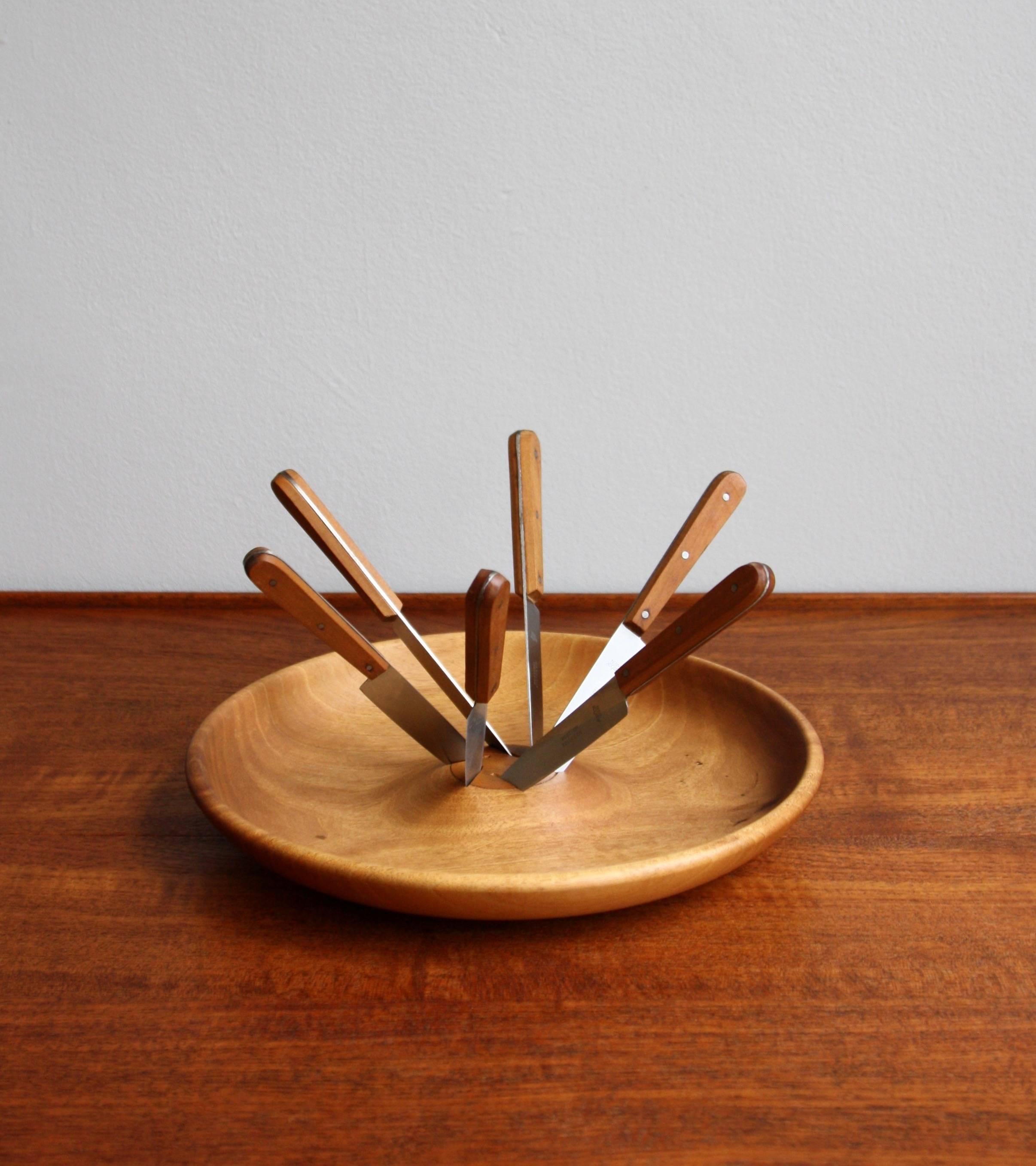 A rare obstmesser/fruit knife set designed and made by Carl Auböck II, circa 1950.
The beautifully grained bowl is carved from a solid piece of walnut wood. A set of six stainless steel knifes with walnut clad handles slot into and spiral outwards