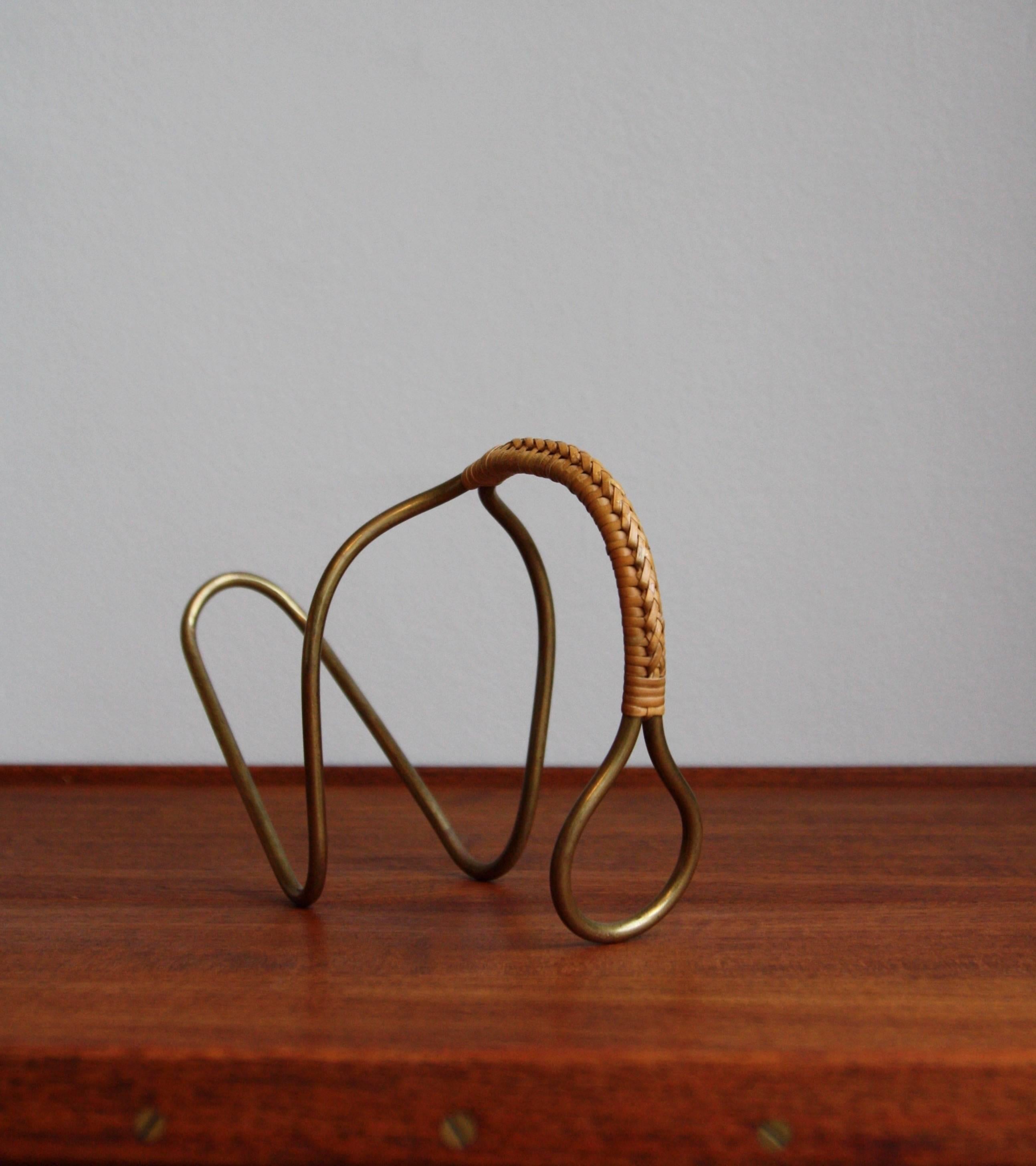 A sculptural bottle holder in solid brass wire and cane designed and made by Carl Auböck II, circa 1950. This device is intended to hold a bottle of wine in a way that helps the wine aerate and the sediment settle.
The patination on both the brass