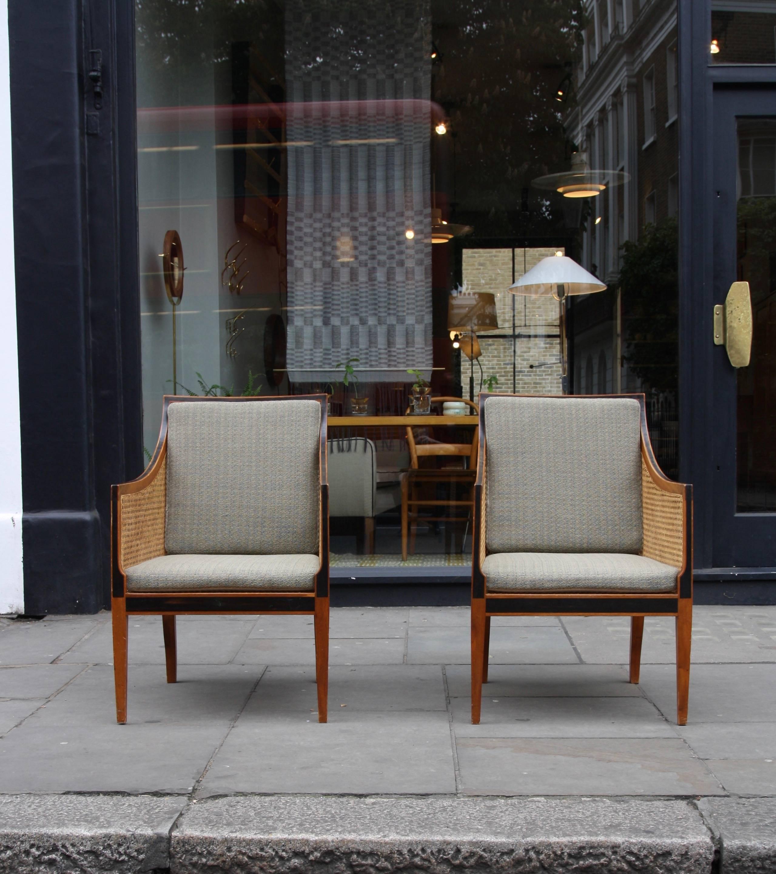 A pair of 'Bergere' or 'English Chairs' designed by Kaare Klint in 1932 and made by the cabinetmaker Rud Rasmussen, Copenhagen, in the early 1940s.

The chairs have solid mahogany frames with rosewood marquetry inlay and woven cane panels to each