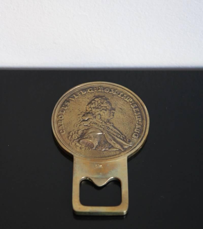 Cast brass bottle opener by the Auböck Werkstätte, Vienna, circa 1960.
The piece is shaped as a coin to which the actual bottle opener is attached; on one side of the coin stands out in relief the image of Charles VI, Holy Roman Emperor right