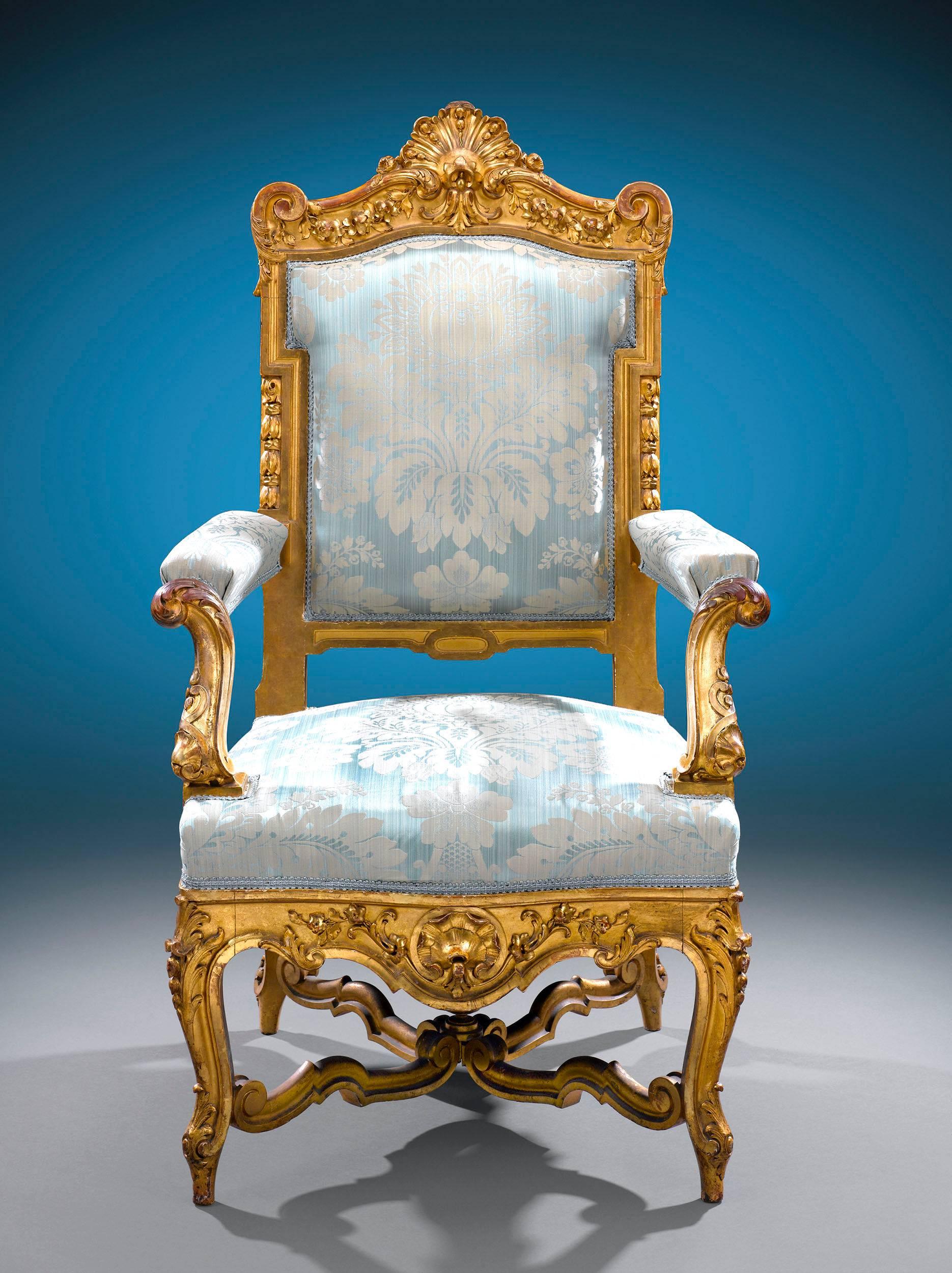 This regal pair of giltwood armchairs exhibits the best of 18th century French design. These stately fauteuils feature grand Louis XIV and Louis XV ornamentation, from the central shell cresting and floral garlands on the high, indented backs to the