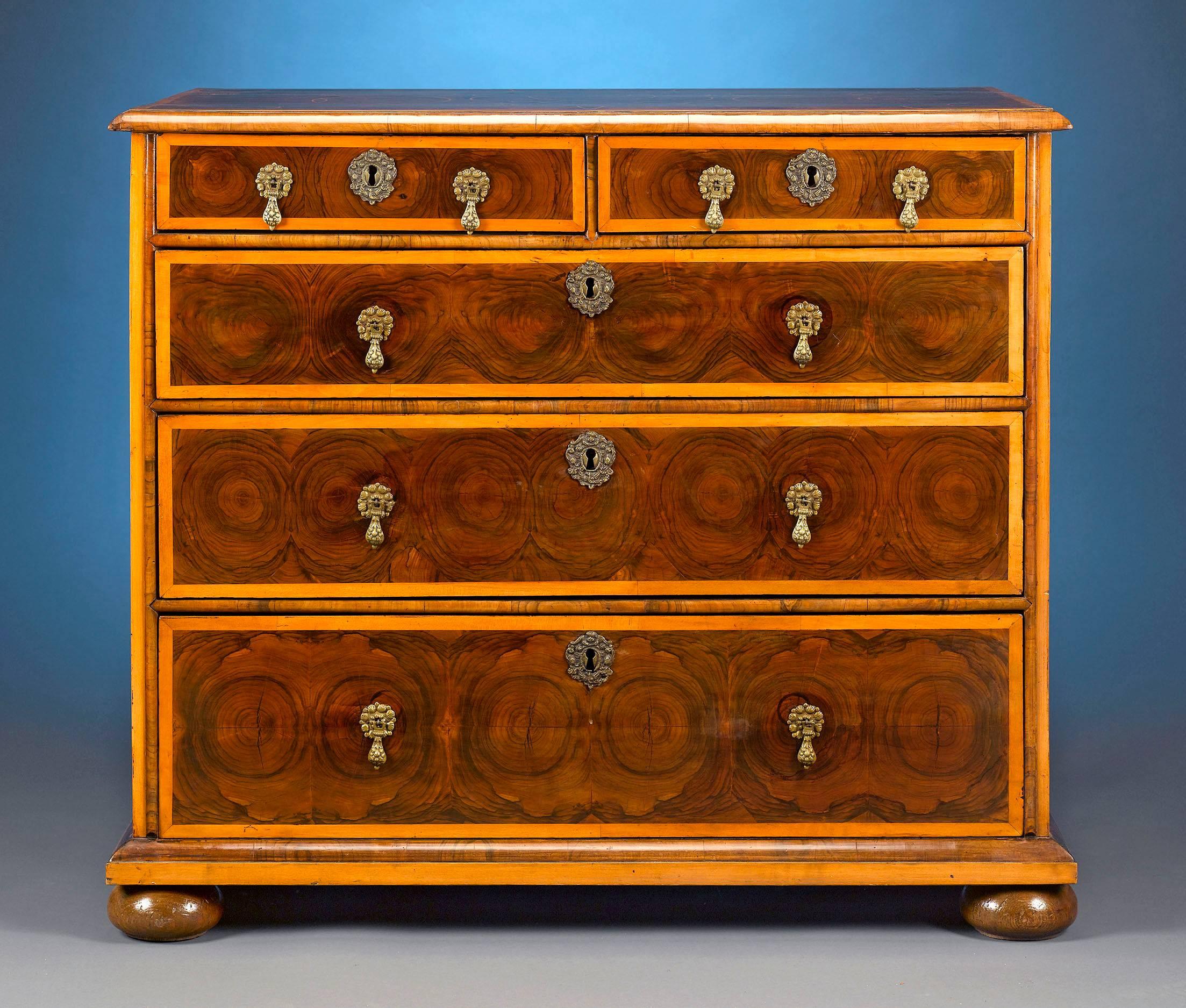 A magnificent William and Mary period chest, clearly distinguished by an expertly applied oysterwood veneer of fine English walnut. From its inlaid top of semi-circular patterns, to its intricate brass pulls and wonderfully curved bun feet, this
