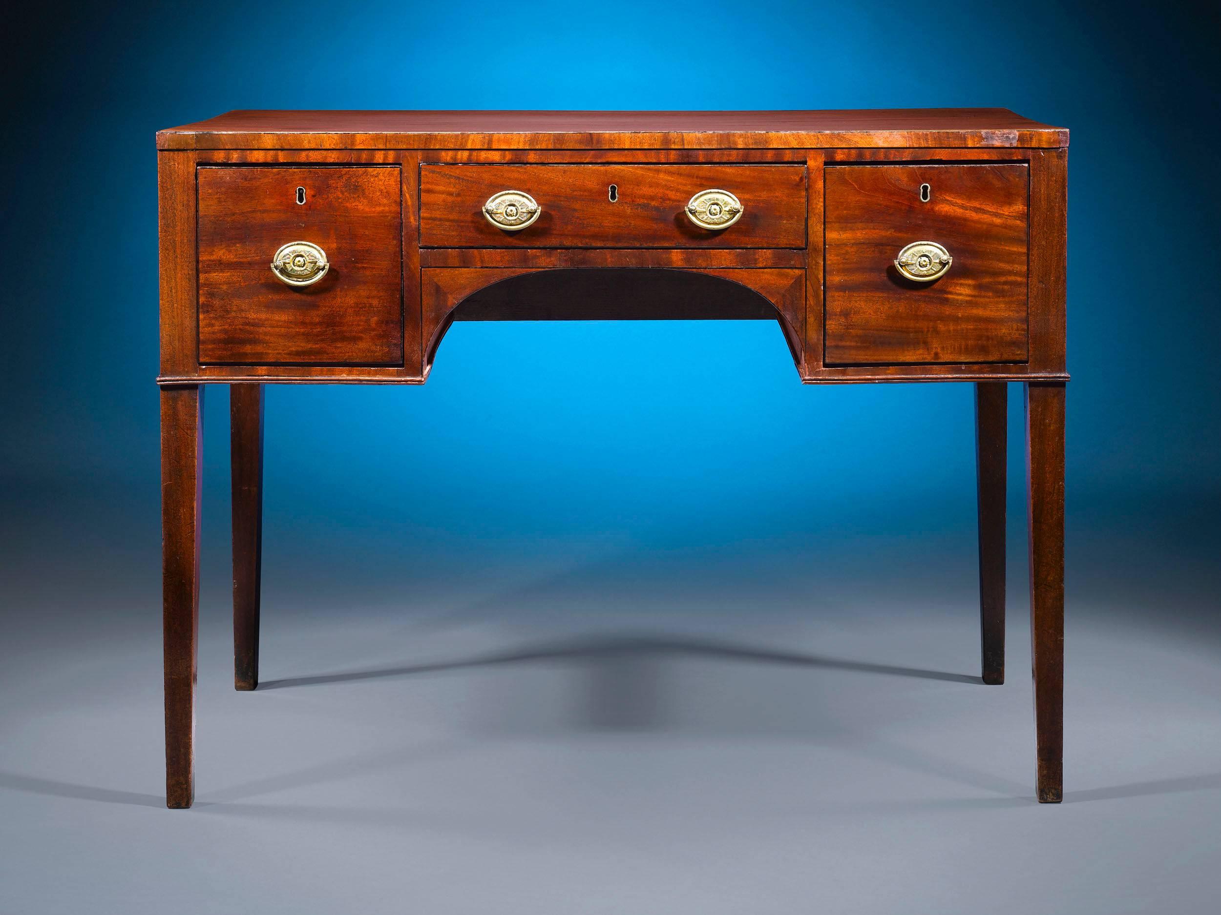 This fine Georgian-era desk is crafted of rich mahogany and features the straightforward design prevalent in England during the early 19th century. Three lockable drawers are adorned with period-style brass pulls, and the desk rests upon tapered