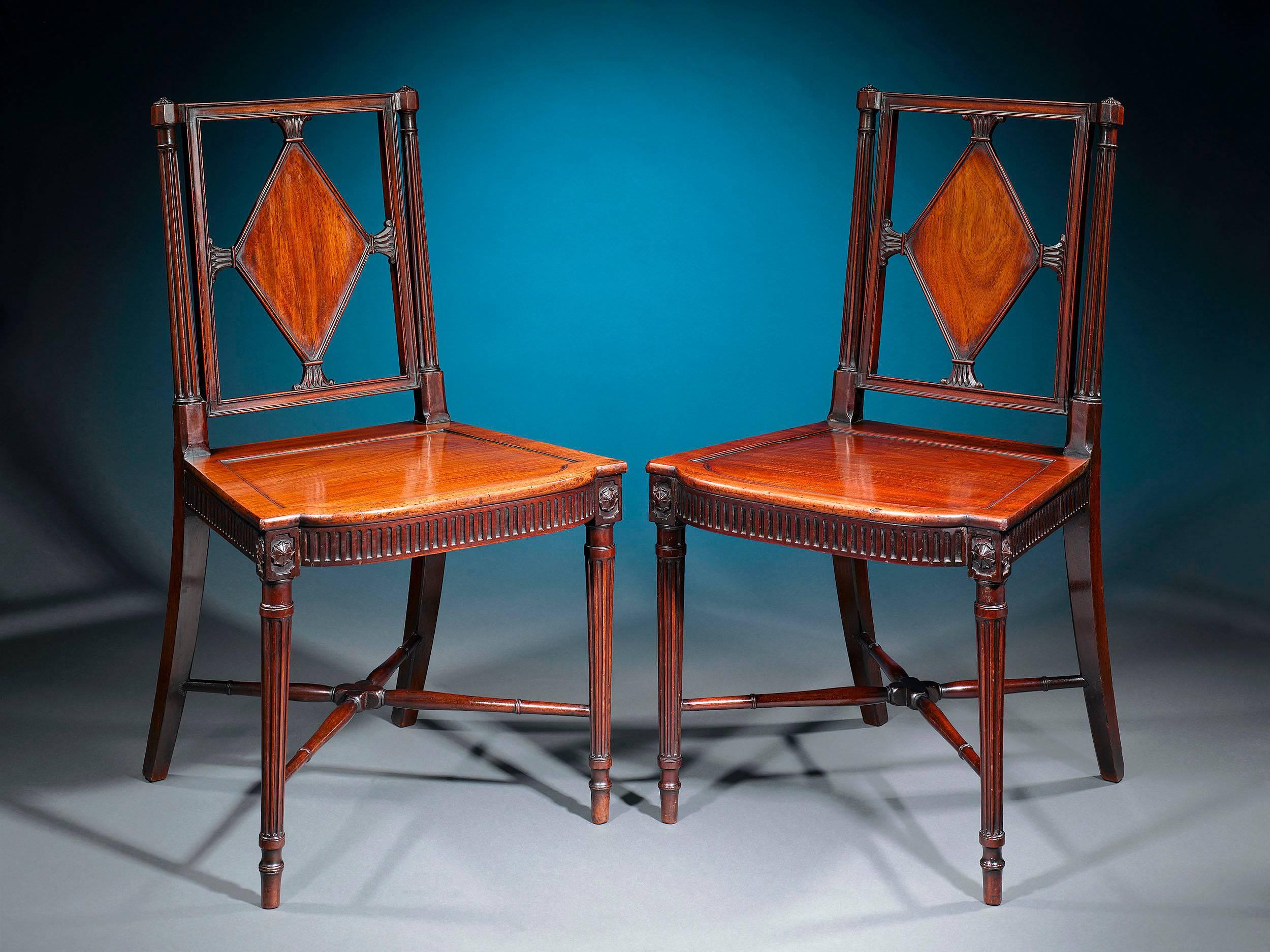 A fine pair of George III era mahogany hall chairs of exceptional craftsmanship and condition. Each masterfully carved seat is constructed with a rectangular back adorned with a lozenge panel between reeded columns. The solid seats are accentuated