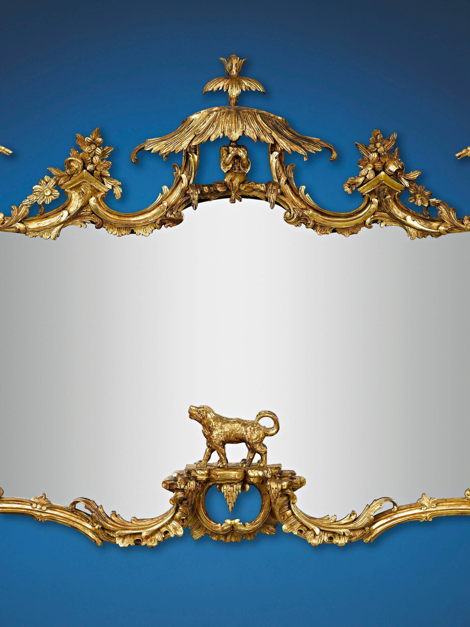 This stunning gilt looking glass is a tour-de-force of chinoiserie and Rococo style. Fashioned in the timeless 18th century style of Thomas Johnson and Thomas Chippendale, the monumental overmantle mirror is adorned by decorative motifs in the