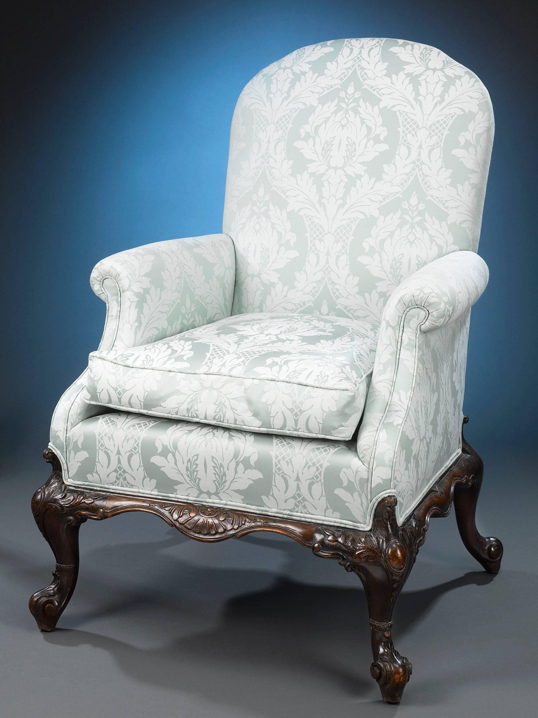 This Classic and highly desirable pair of George II-style armchairs is crafted of luxurious Cuban mahogany. Their large, yet elegant design is bolstered by beautifully upholstered arms, seats and backs, and fully carved cabriole legs reminiscent of