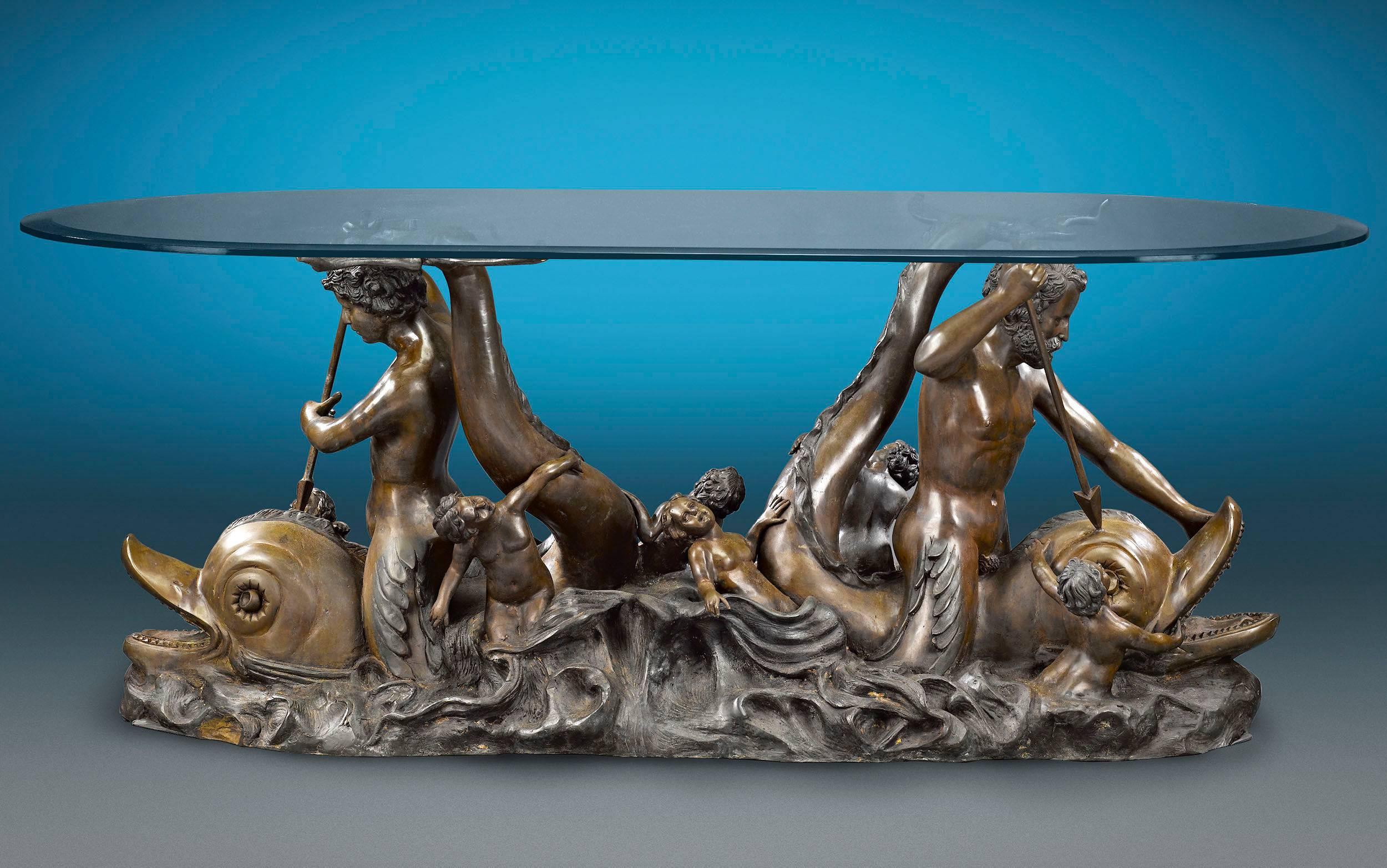 A merman and mermaid are astride a pair of dolphins in this incredible bronze sculptural table. As the merpeople spear their pray, they are joined by several putti enveloped by tumultuous waves. Its sleek glass top allows the opulent bronze to be